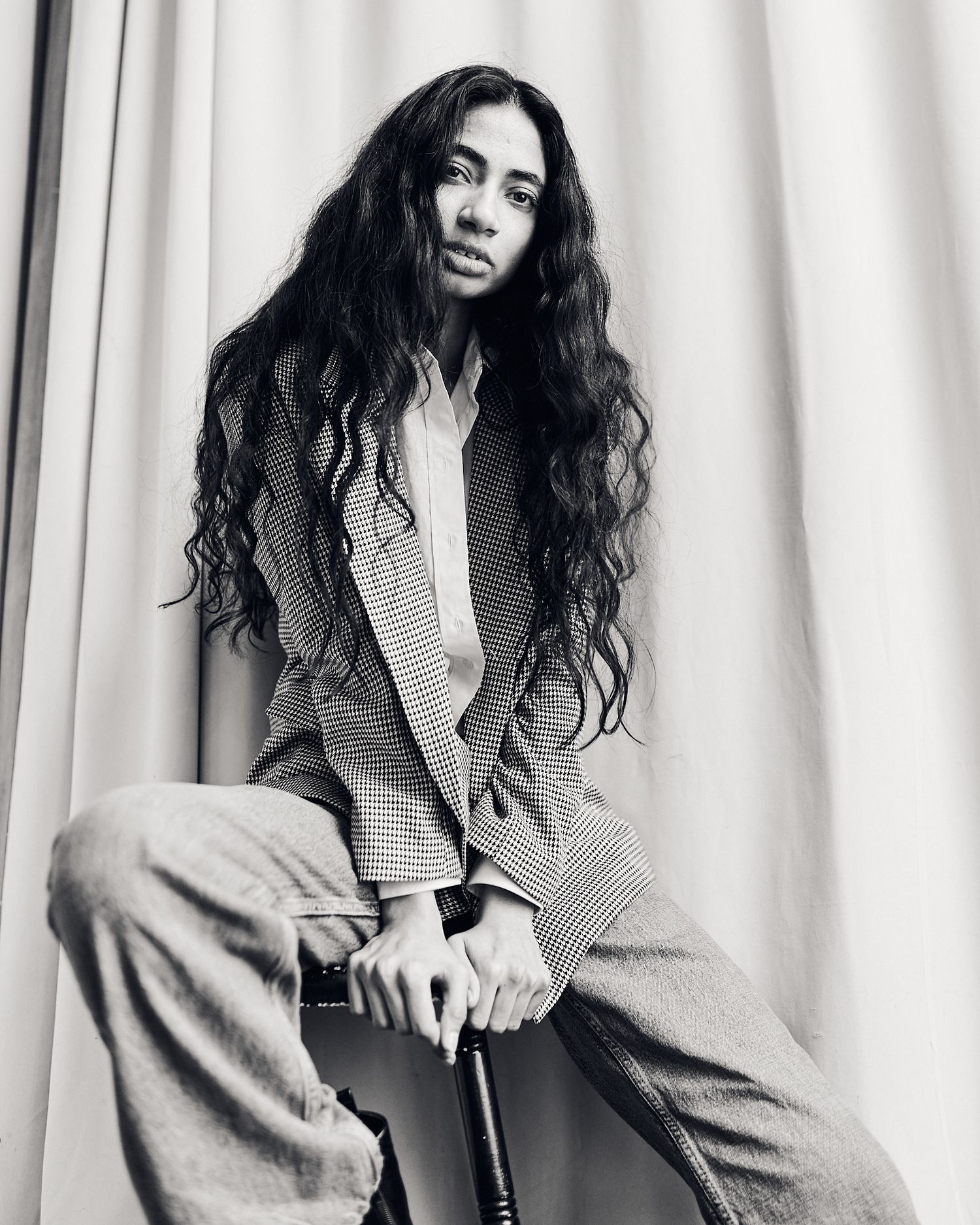 Black and white portrait showing long wavy hair and checkered blazer with wide-leg pants.