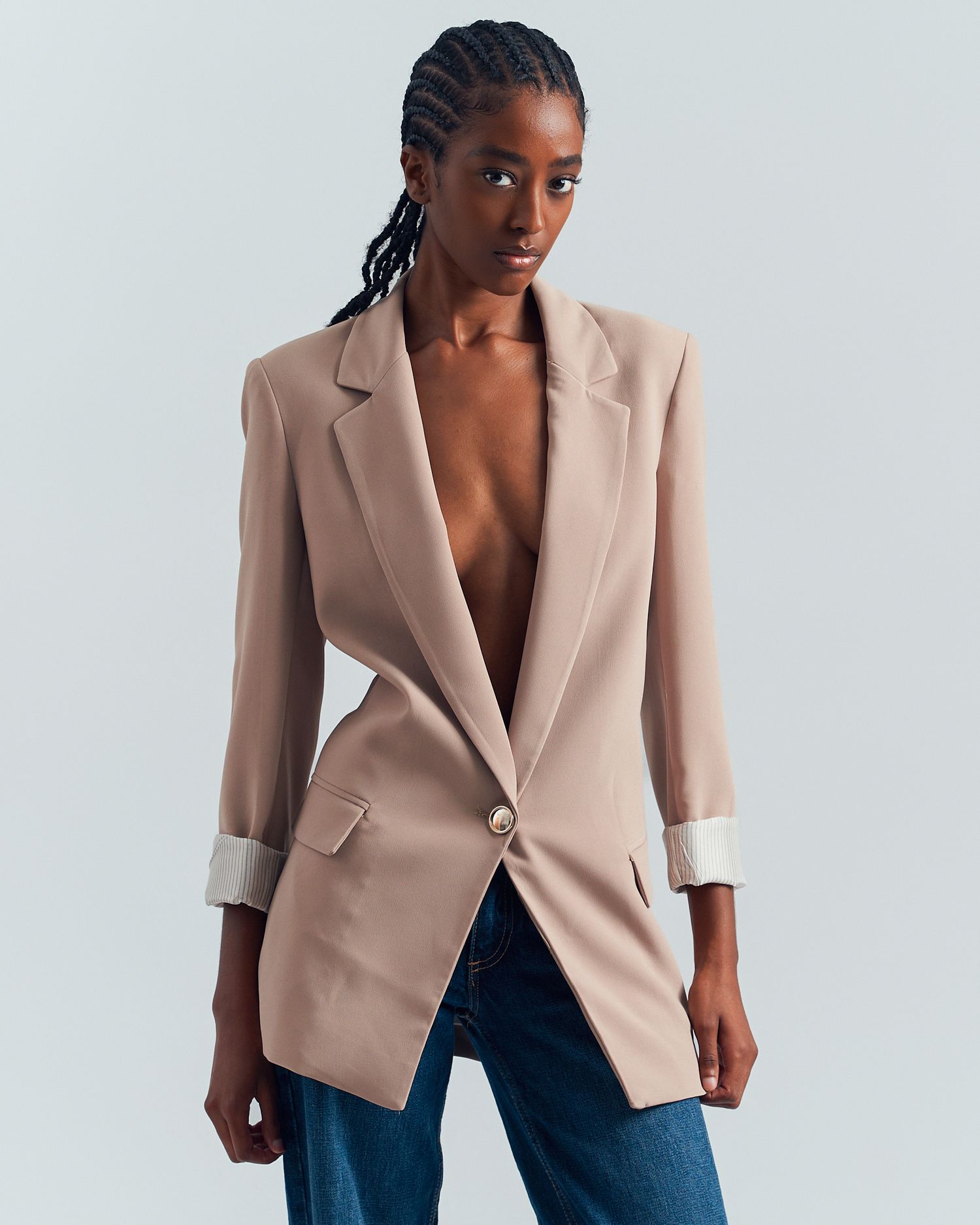 Model wearing a beige blazer and dark jeans poses against white background in four different angles.