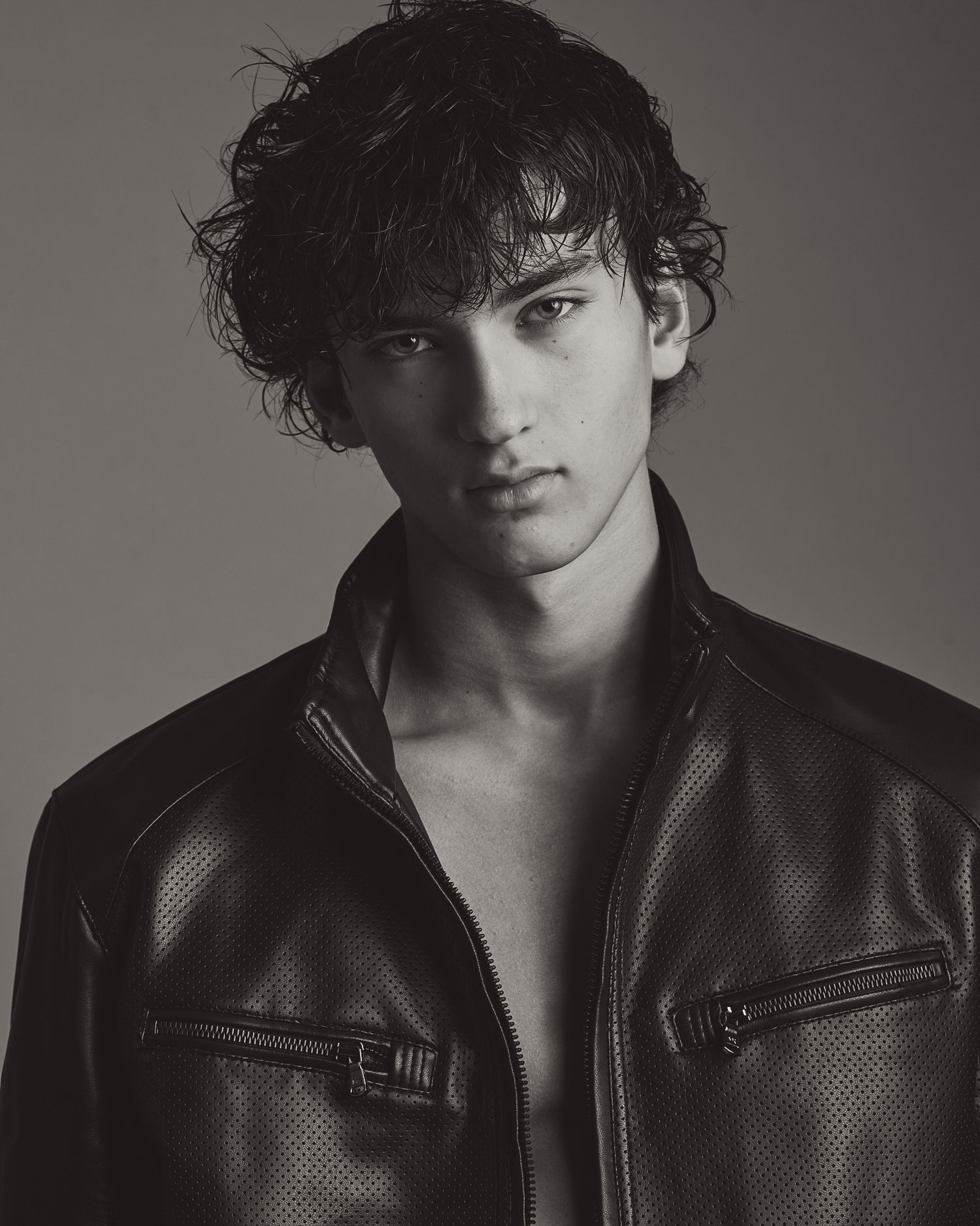 Black and white fashion portrait series showing dramatic side angles in a leather jacket against a gray backdrop.