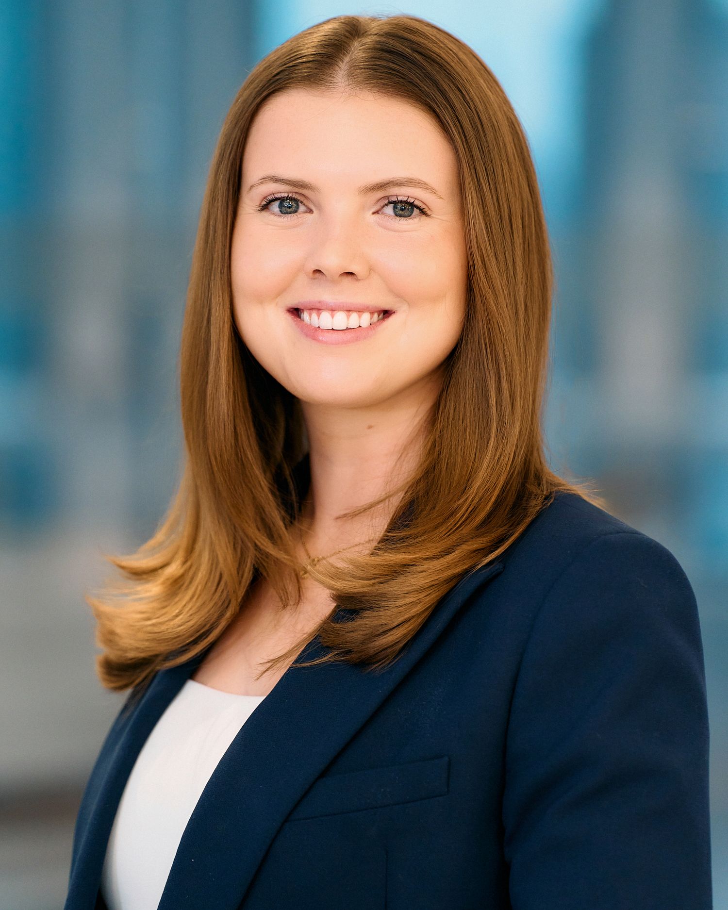 Professional headshot portrait of someone in a navy blazer and white top against a blue background.