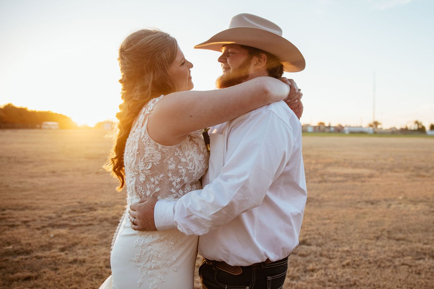 A romantic sunset embrace between newlyweds in a rustic outdoor setting.