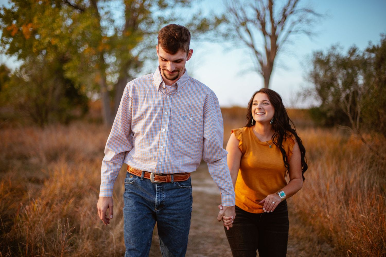 A couple walks together through autumn grass during a casual outdoor photoshoot.