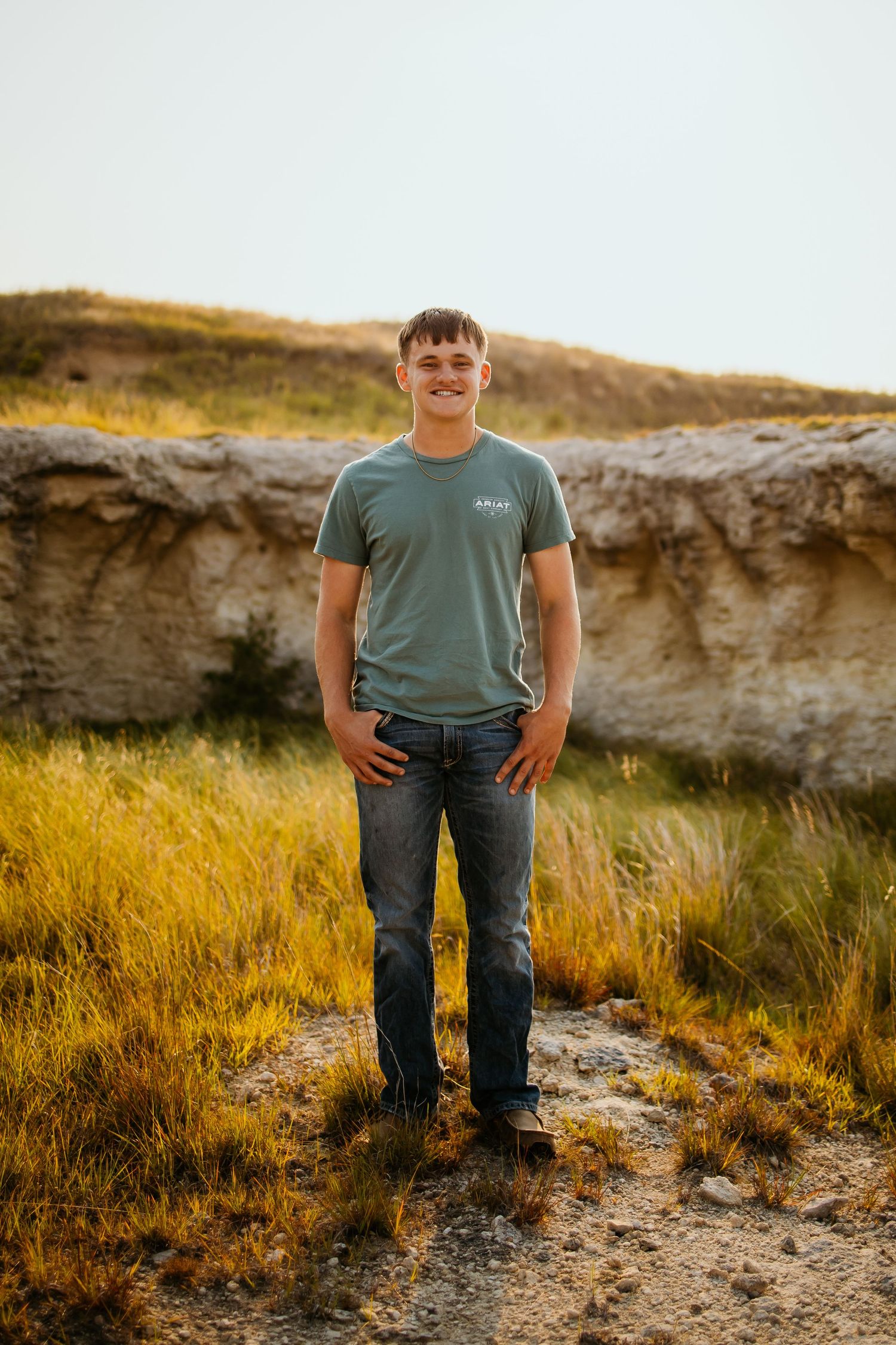 Person stands on rocky terrain against golden grasses and limestone cliffs at sunset.