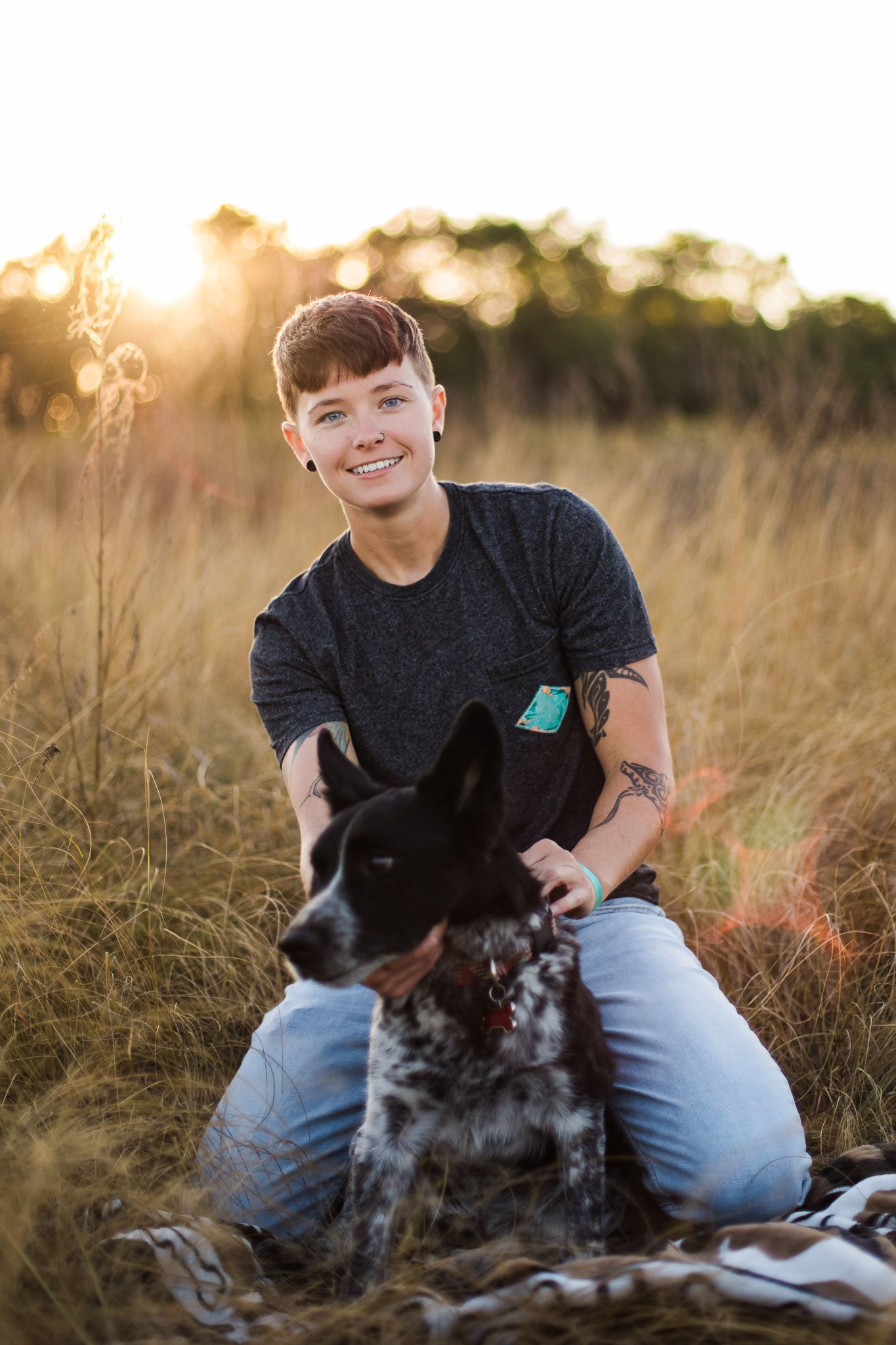 Person and spotted dog share tender moment in sunlit grassy field at golden hour.