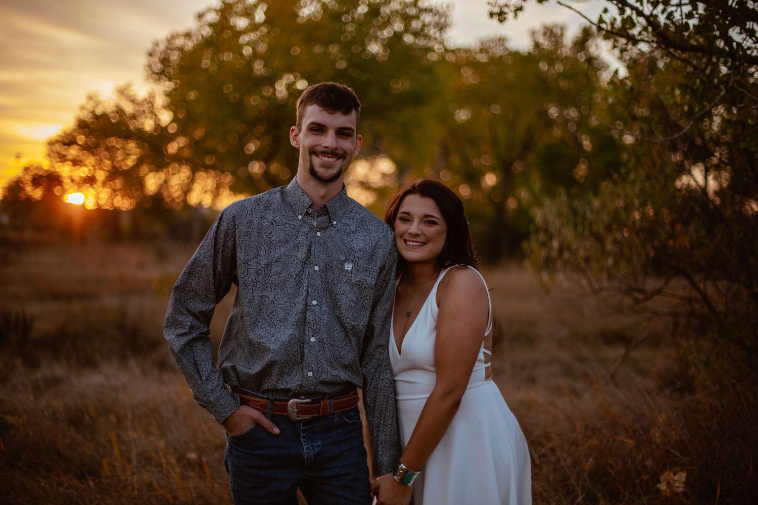 A couple poses together at sunset in a rustic field setting.