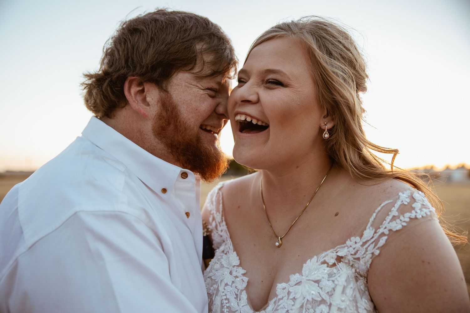 Newlywed couple laughs together during sunset photo session in wedding attire.
