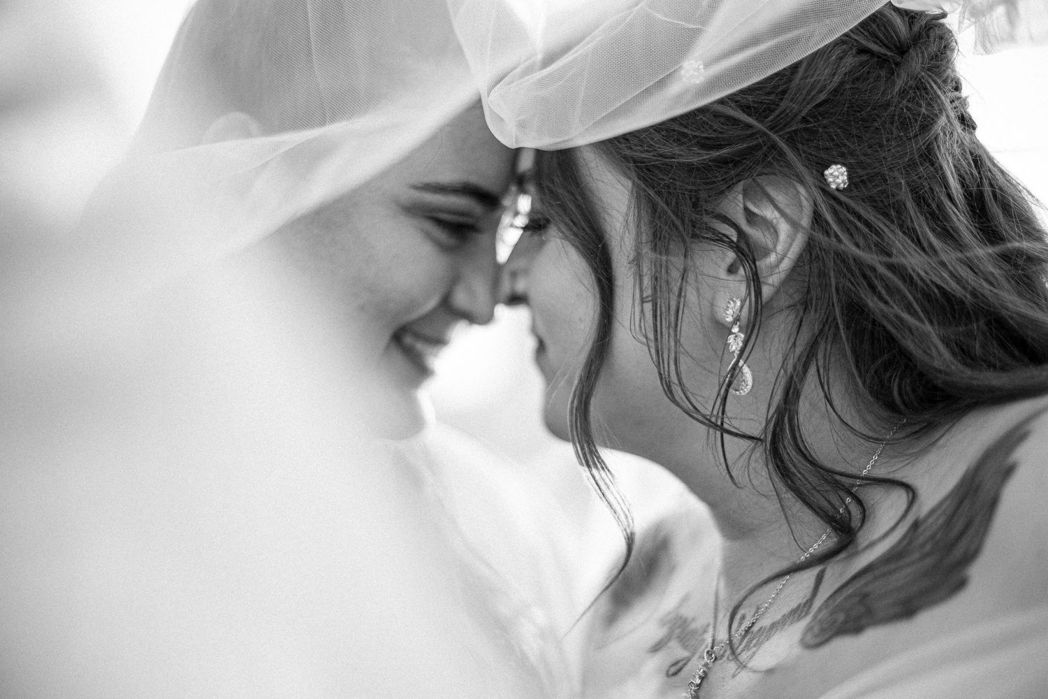 A black and white close-up of two people touching foreheads through a delicate veil.