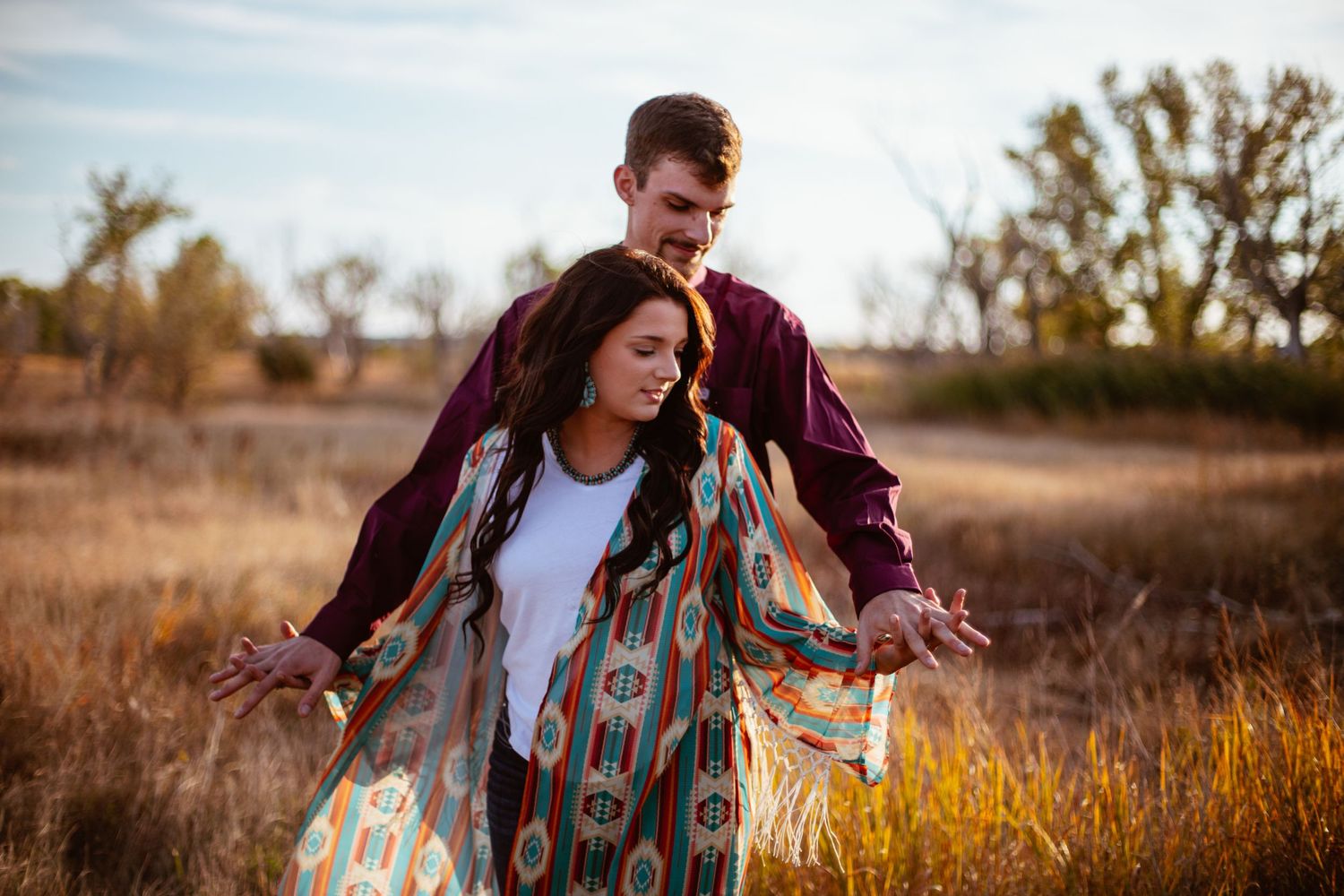 A couple shares a playful moment in a golden autumn field at sunset.