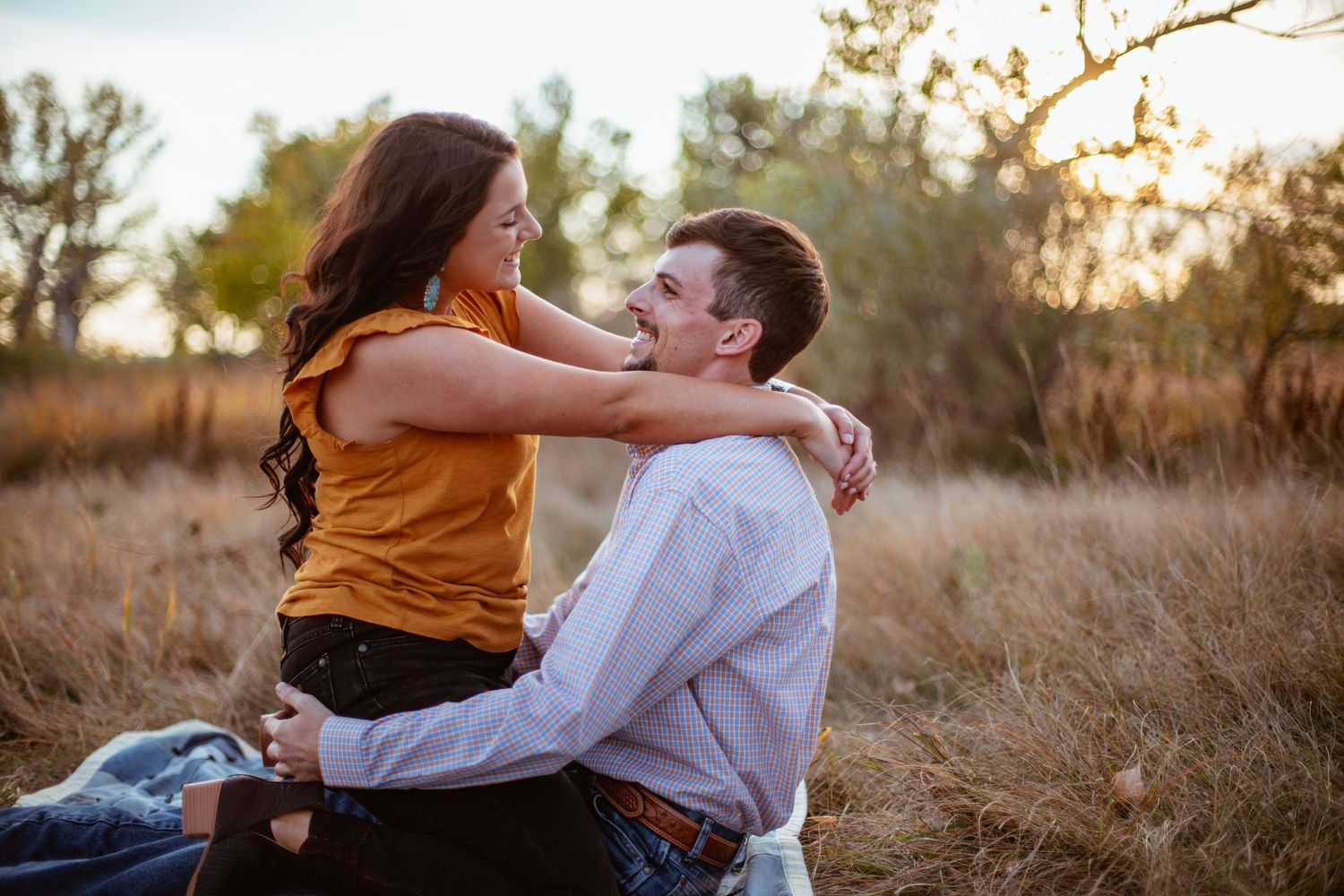 Couple embracing intimately in rustic field at golden hour.