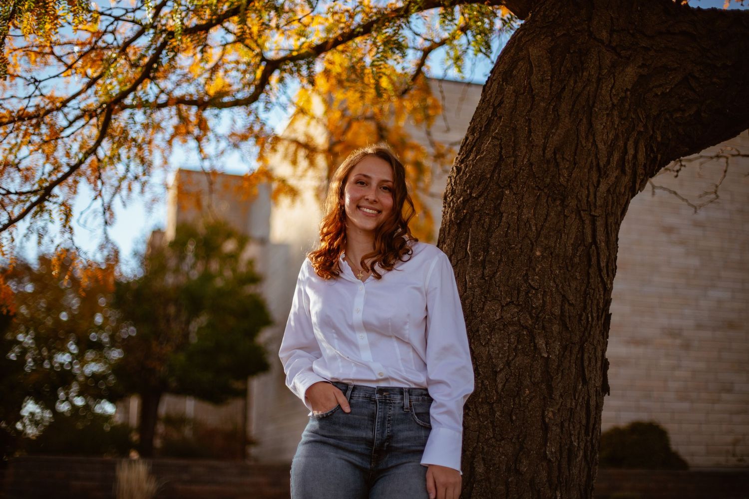 Portrait against autumn tree with golden sunlight filtering through branches.