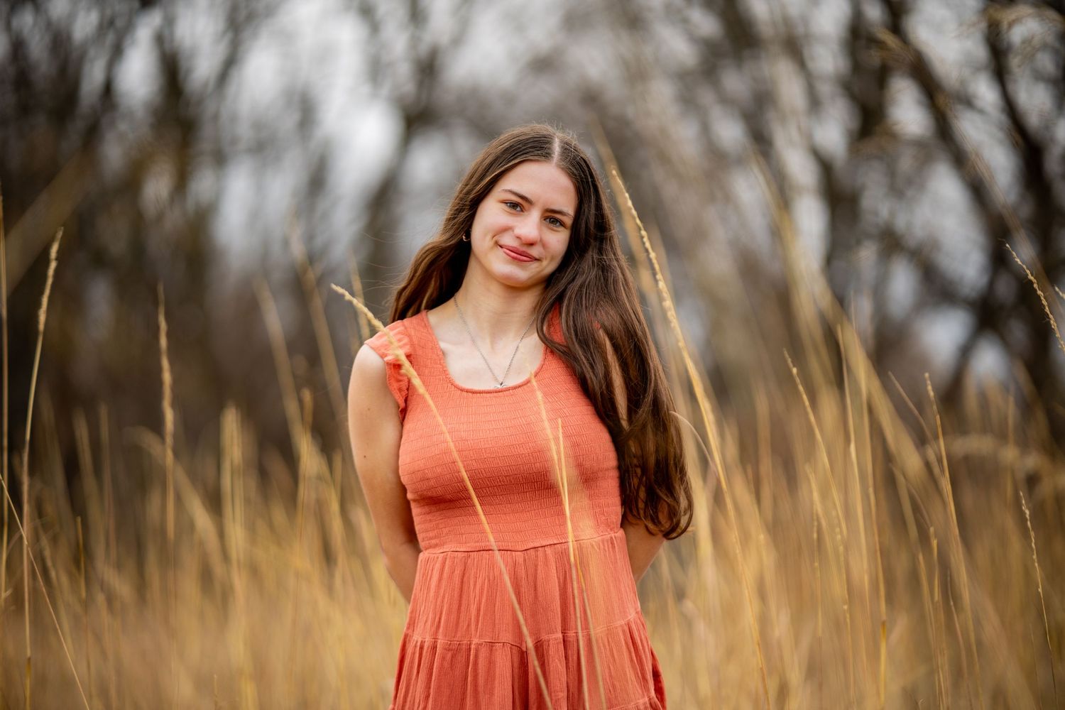 Woman in coral dress stands in tall prairie grass during golden hour.