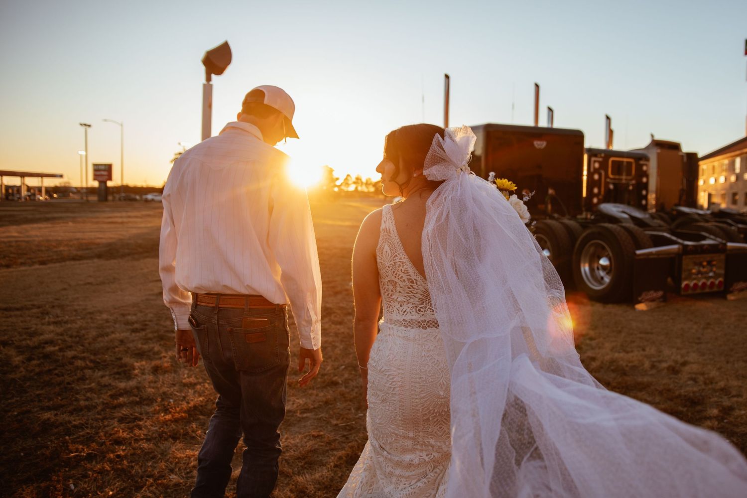 Newlyweds walking together at golden hour with dramatic sunburst behind them.