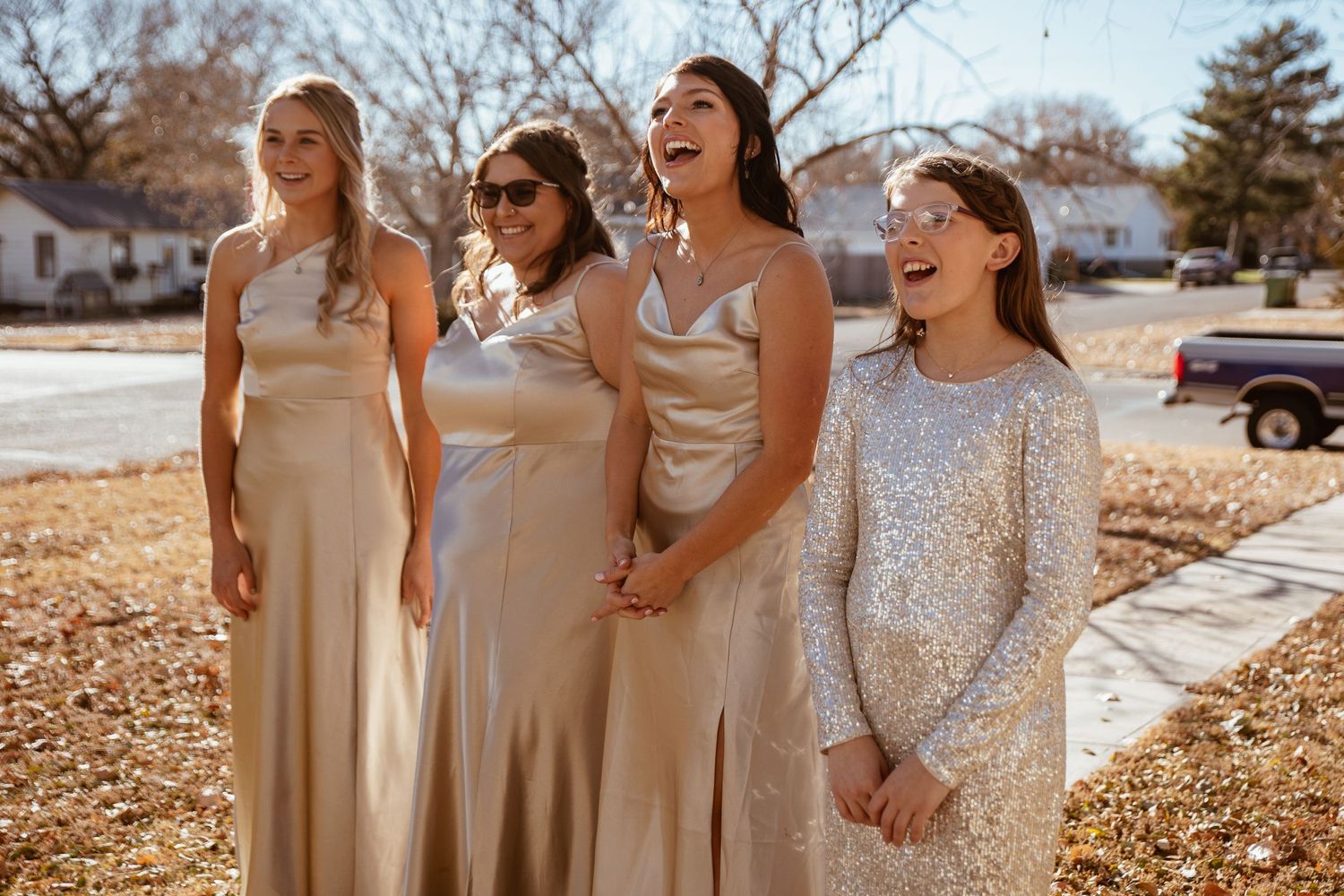 Wedding party in champagne and sparkly dresses share a laugh outdoors.