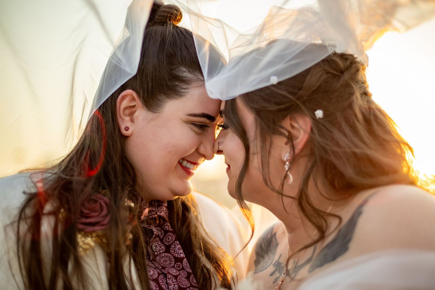 Two people share an intimate moment in golden sunlight with a flowing veil.