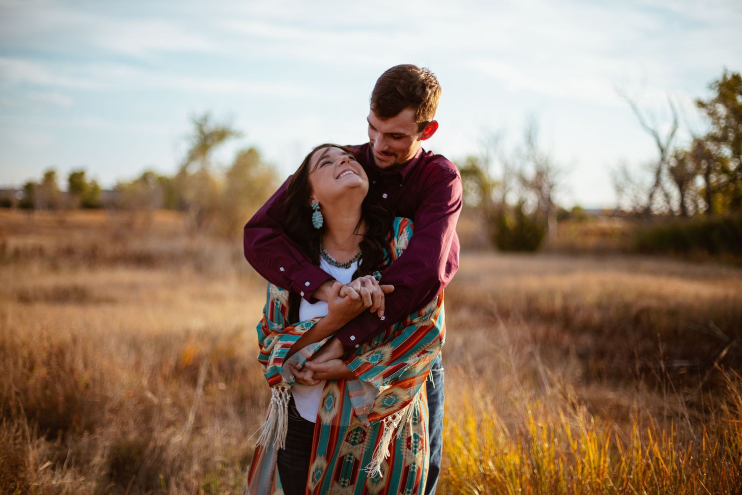 A romantic couple embraces in a golden field during sunset creating an intimate moment.