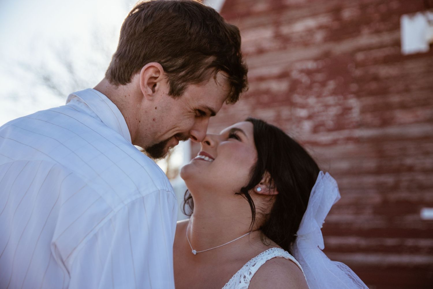 Intimate close-up of couple sharing tender moment against red brick wall.