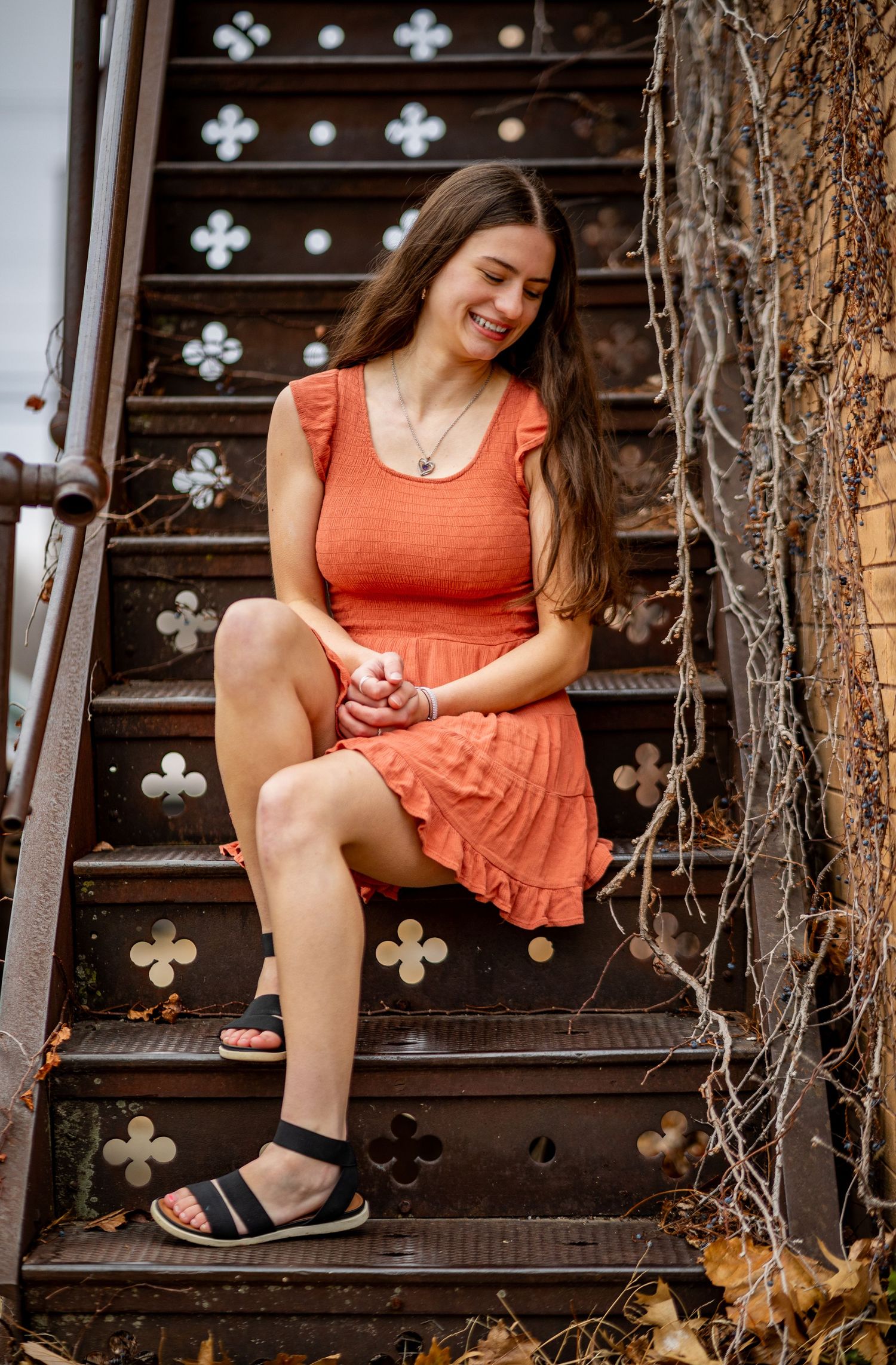 Woman in coral summer dress sits on decorative metal stairs with clover designs.