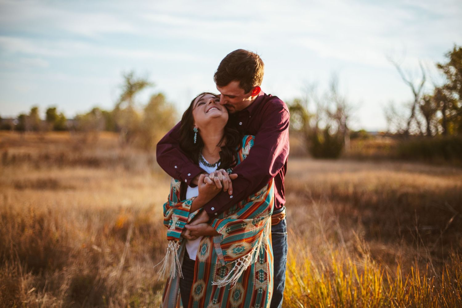 Couple sharing intimate moment wrapped in patterned blanket at sunset.