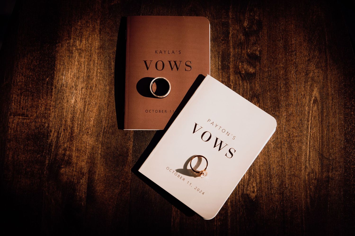 Two wedding vow books with ring designs on wooden surface.