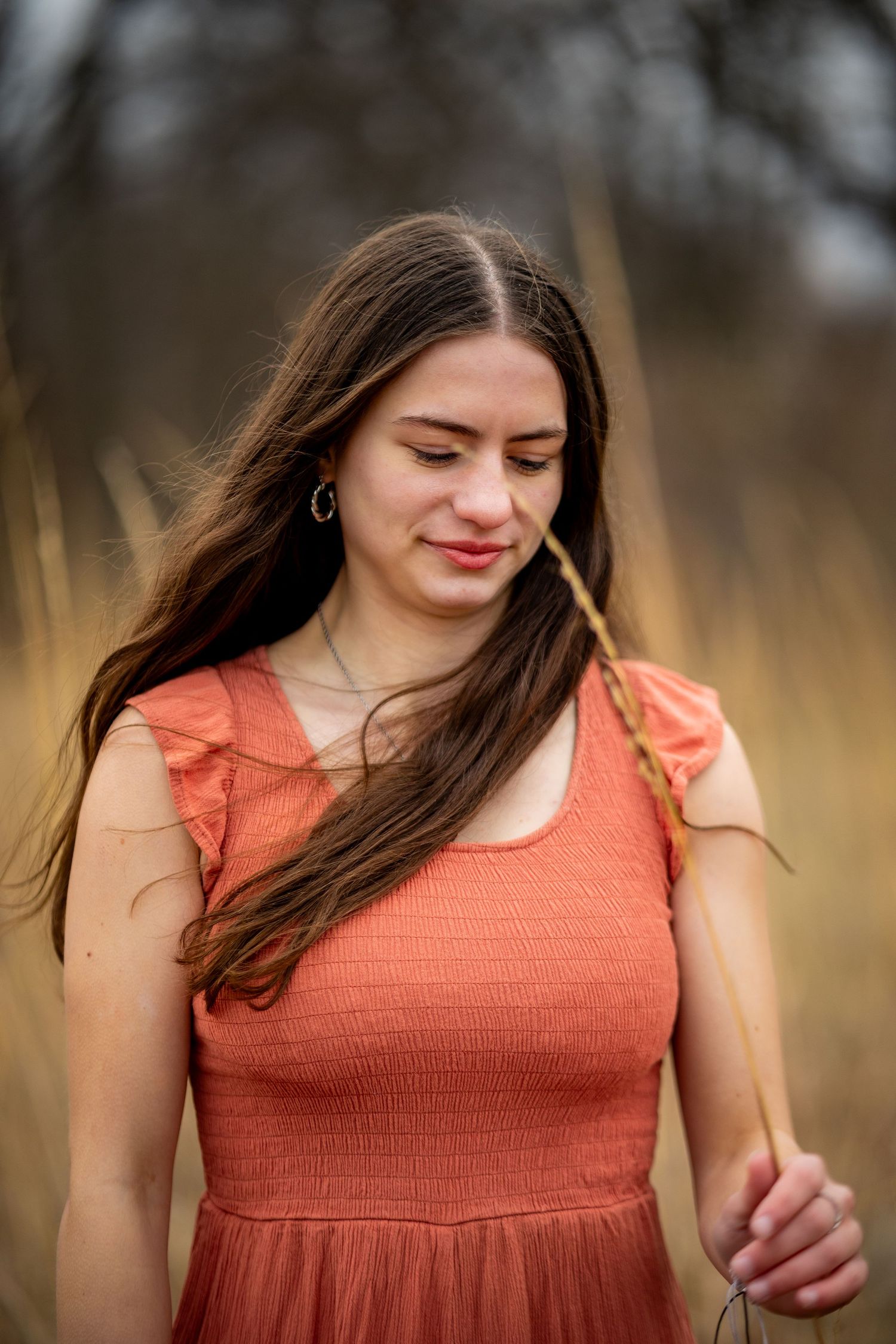 Woman in coral dress poses thoughtfully in autumn field.