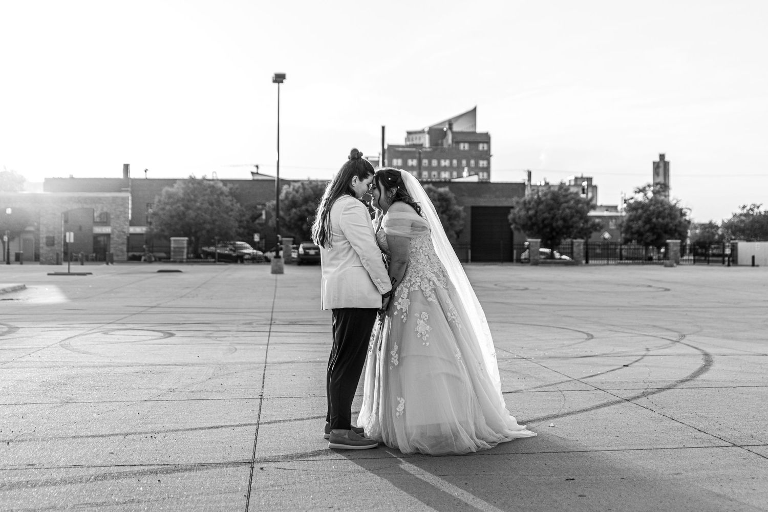 A romantic black and white wedding photo of a couple embracing in an urban setting at sunset.