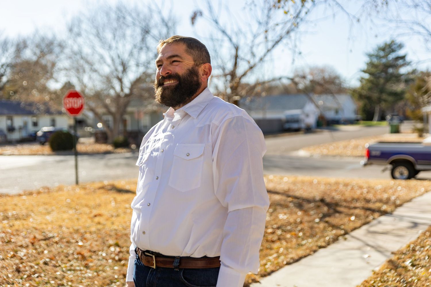 Man in white dress shirt and jeans smiling outdoors on a sunny day.
