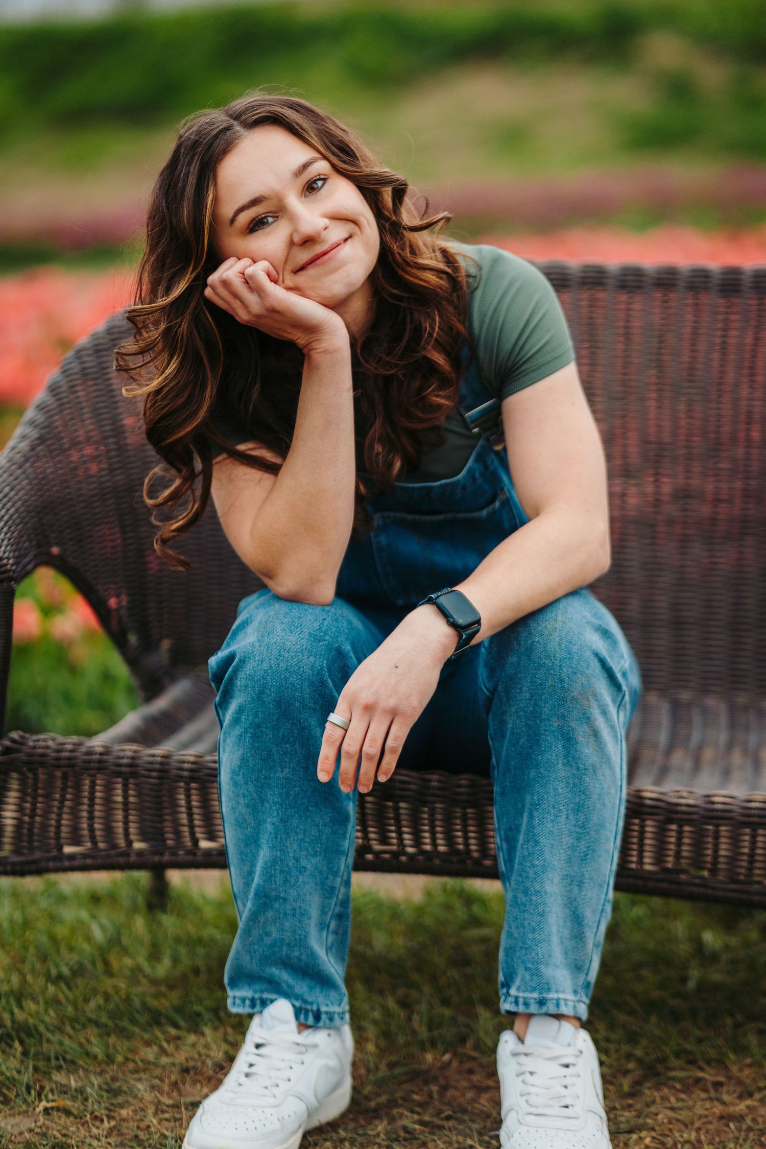 Person wearing casual jeans and white sneakers sits on woven outdoor furniture in lush garden setting.