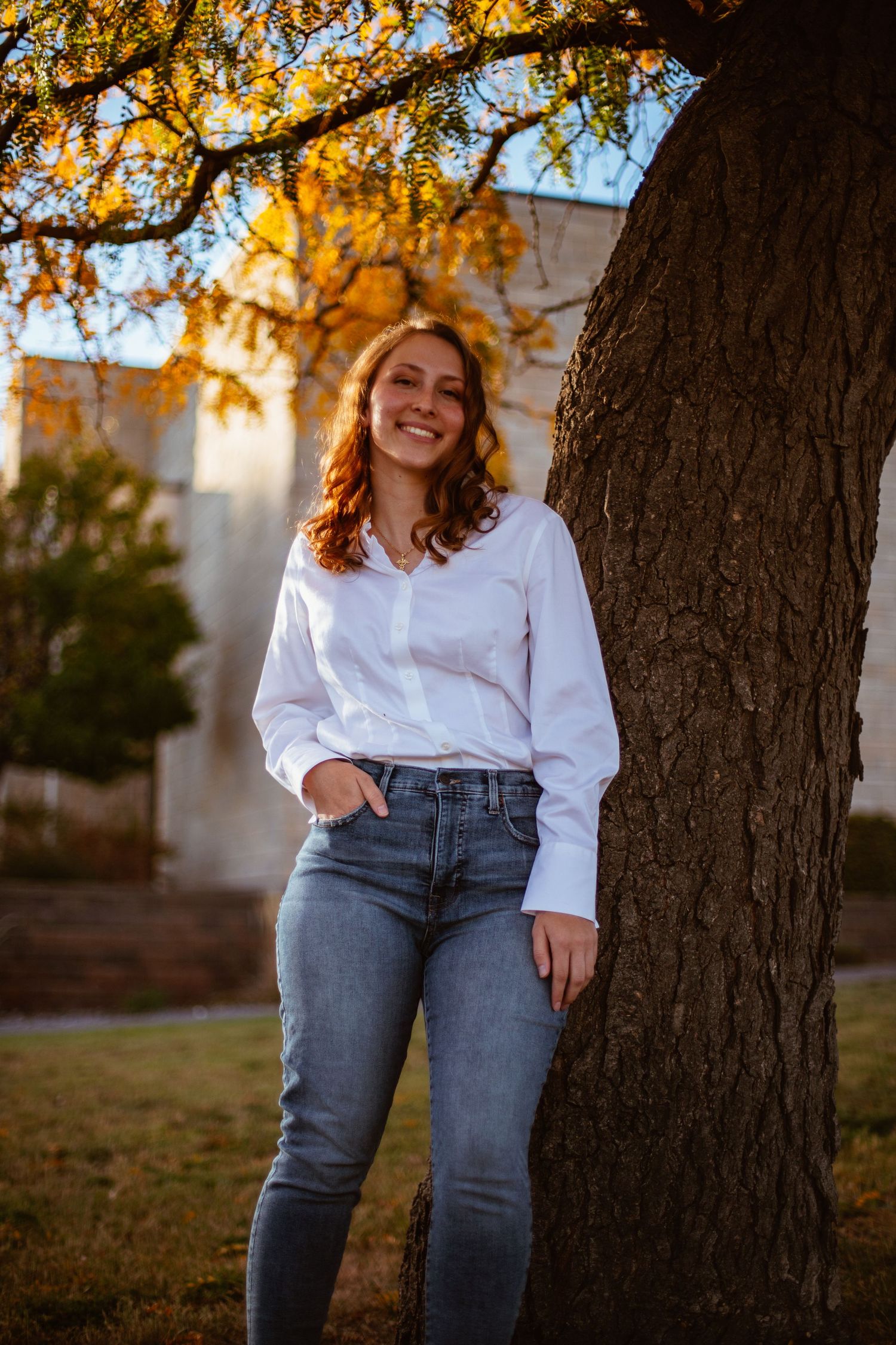 Casual portrait against a tree trunk with golden autumn foliage in the background during sunset.