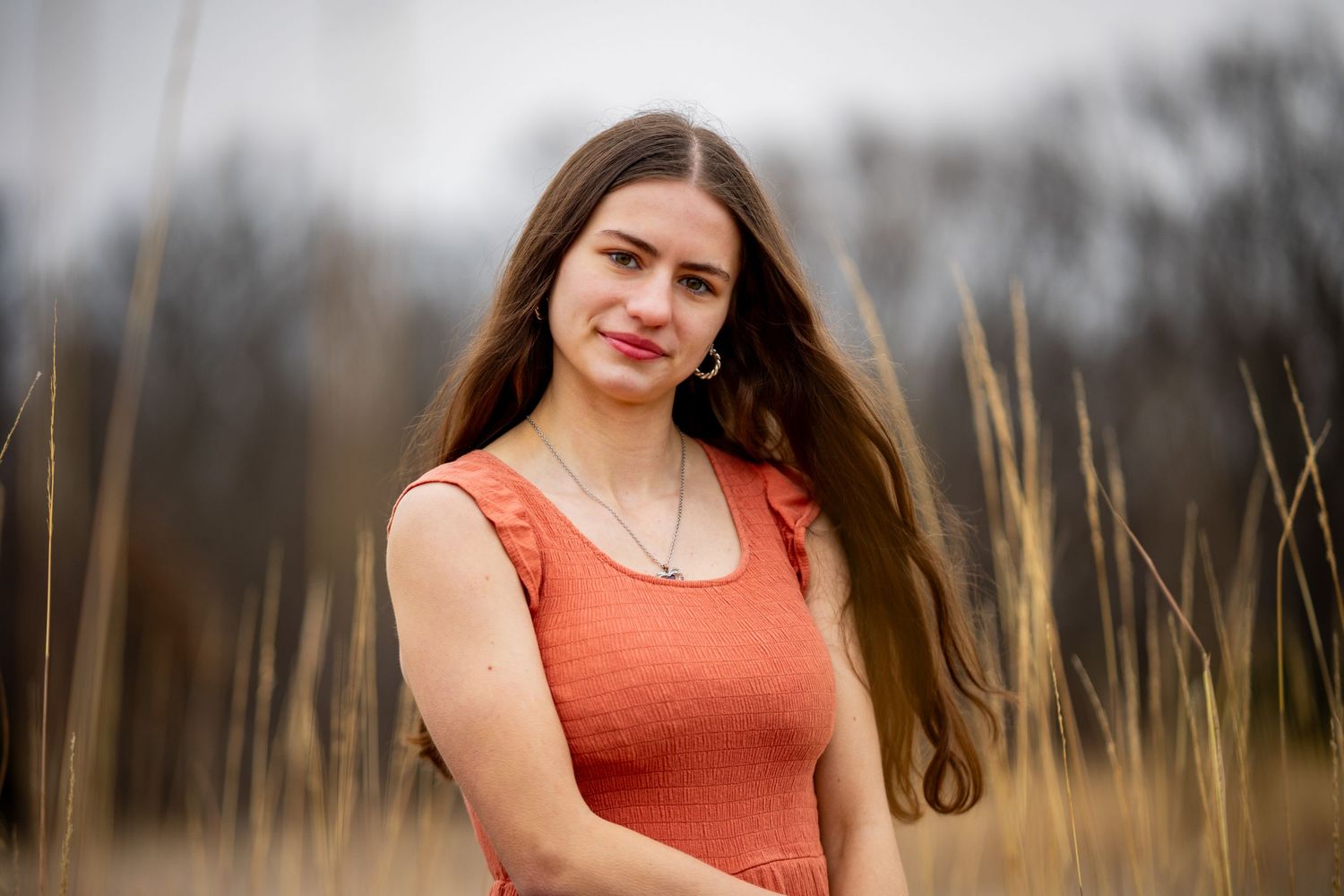 Portrait in golden field shows person in coral tank top with flowing dark hair.
