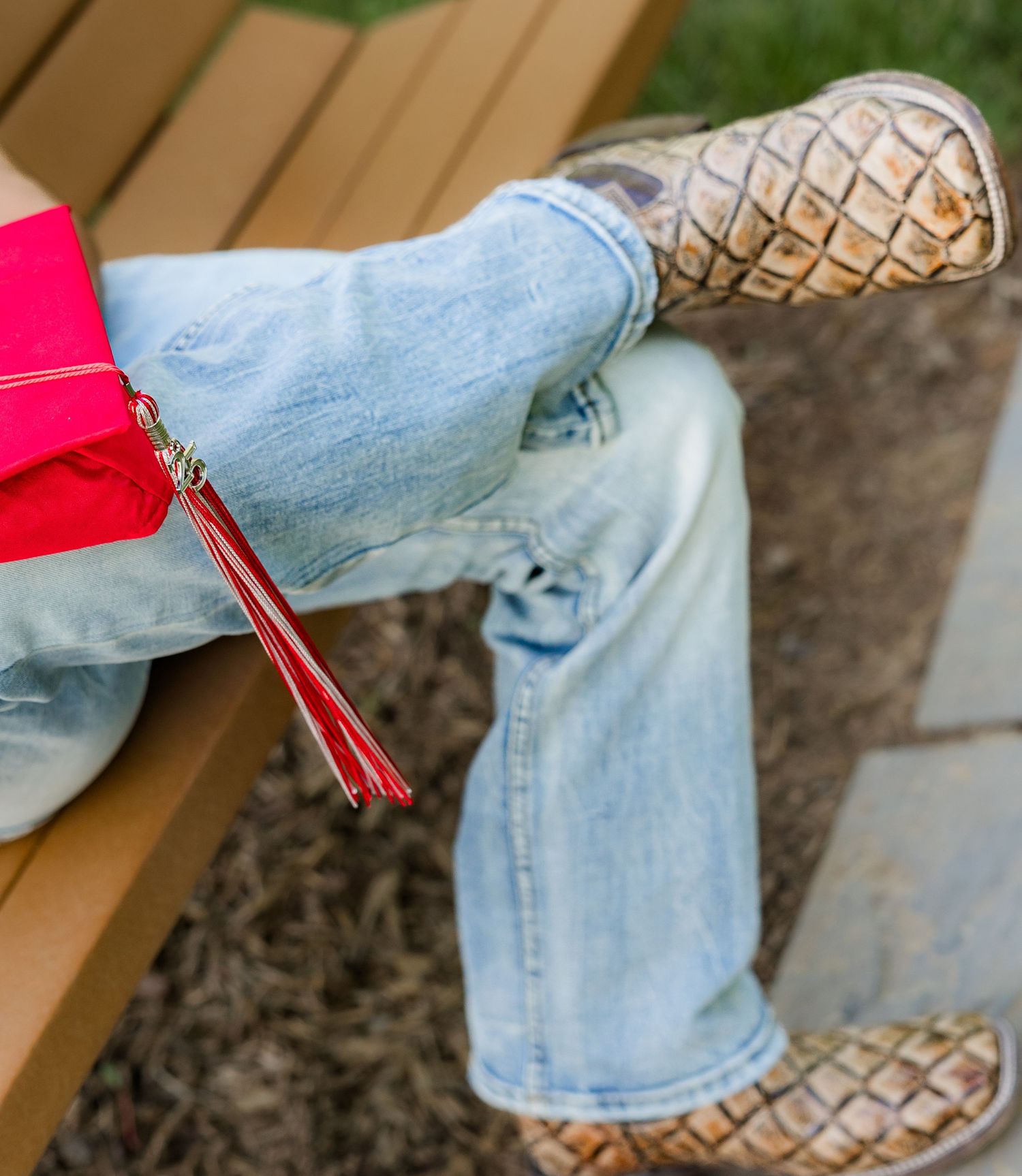 Close-up of light blue jeans with a decorative red tassel detail.