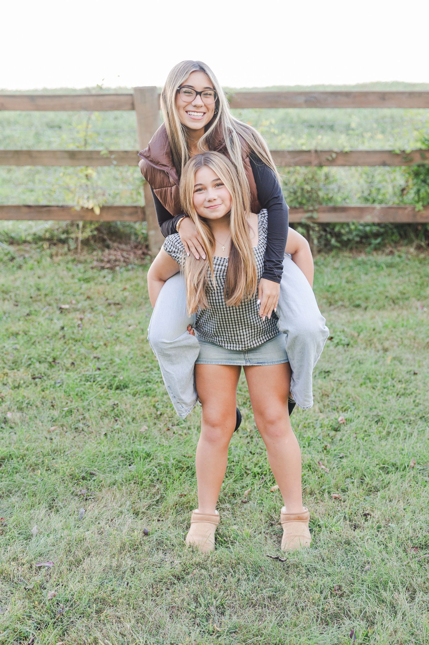Two friends having fun with piggyback ride in front of rustic wooden fence outdoors.