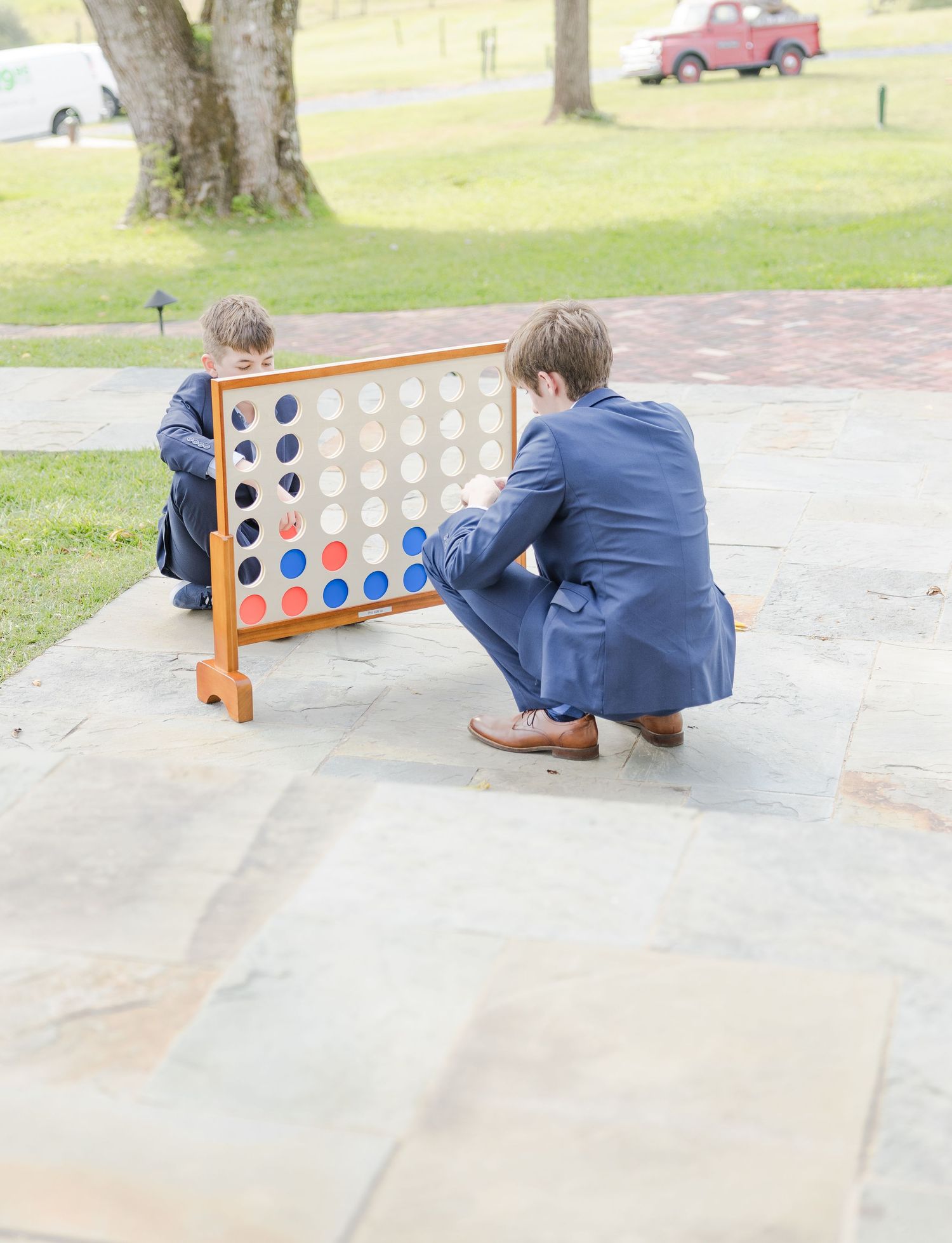 Two people in blue suits playing a large outdoor Connect Four game.