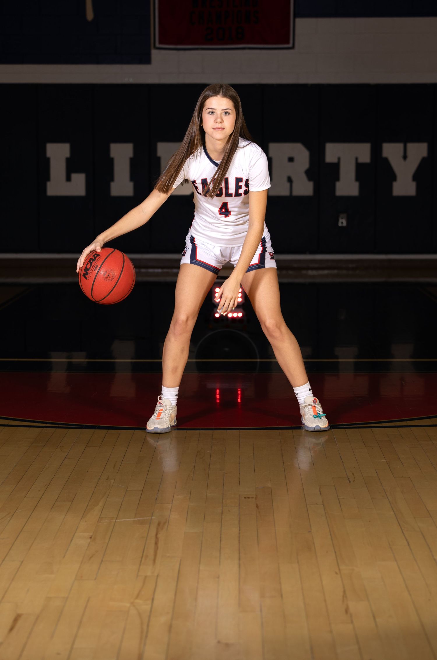 Basketball player dribbles in defensive stance on wooden court.