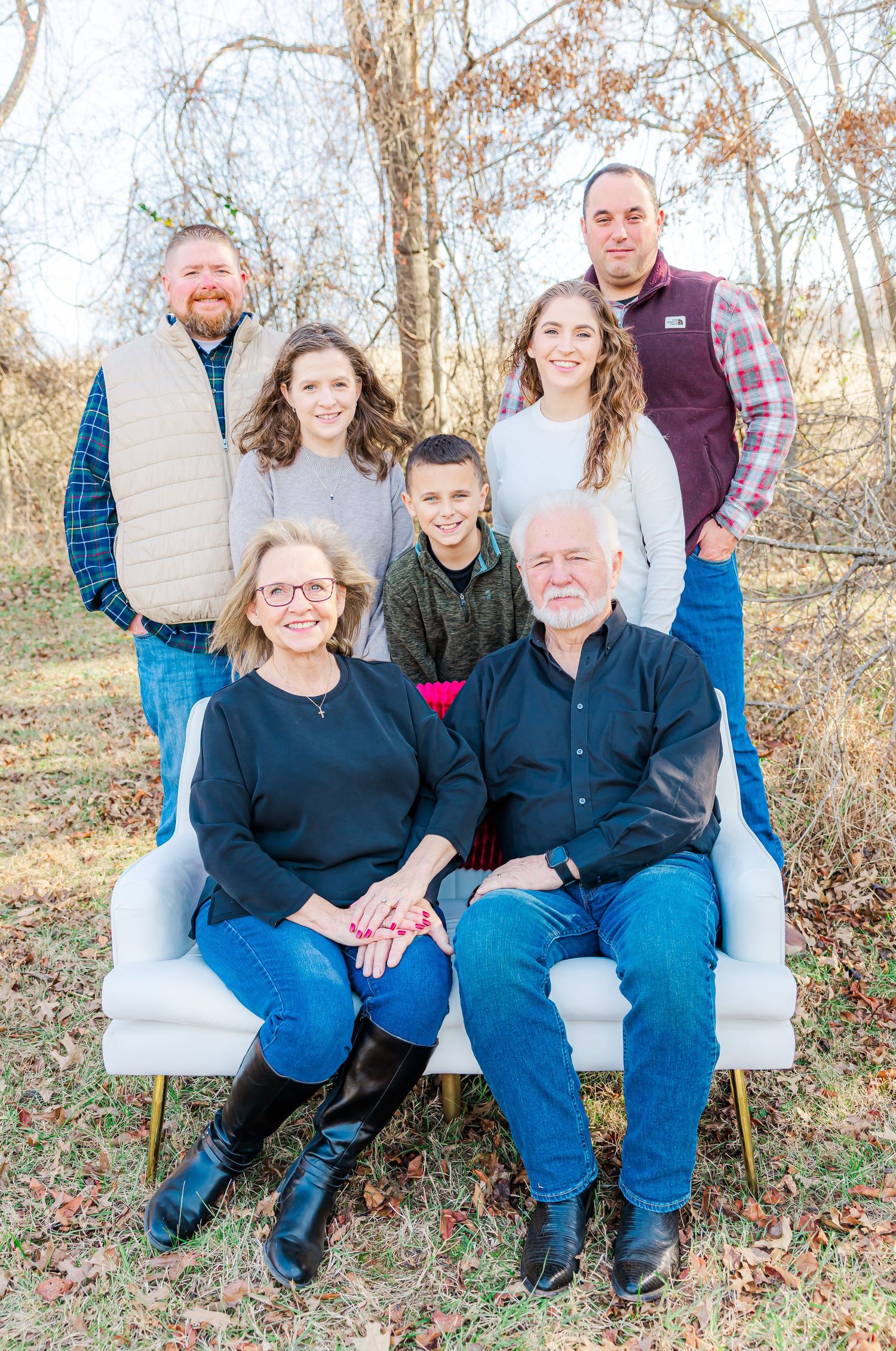 Extended family members pose together on white furniture for outdoor portrait photographs.