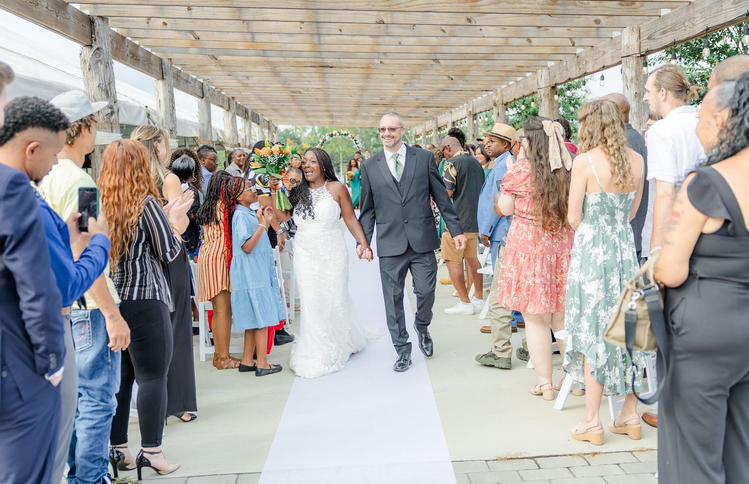 Wedding reception guests mingle under covered outdoor pavilion.