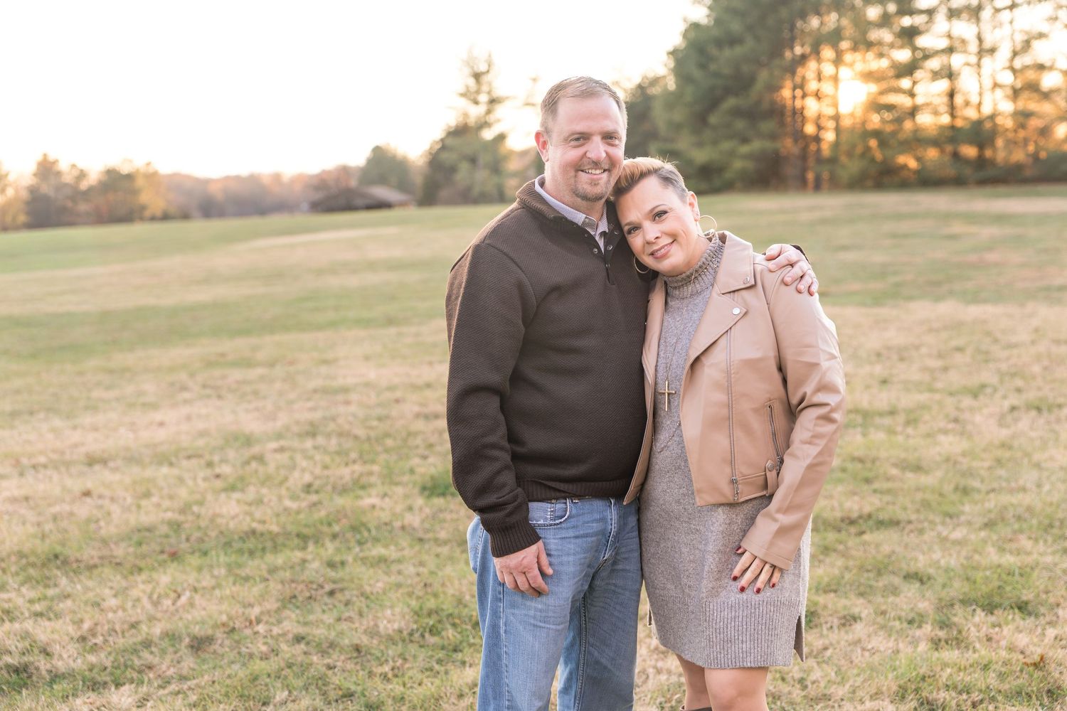 Two people embrace while standing in a golden field at sunset during a fall photo session.