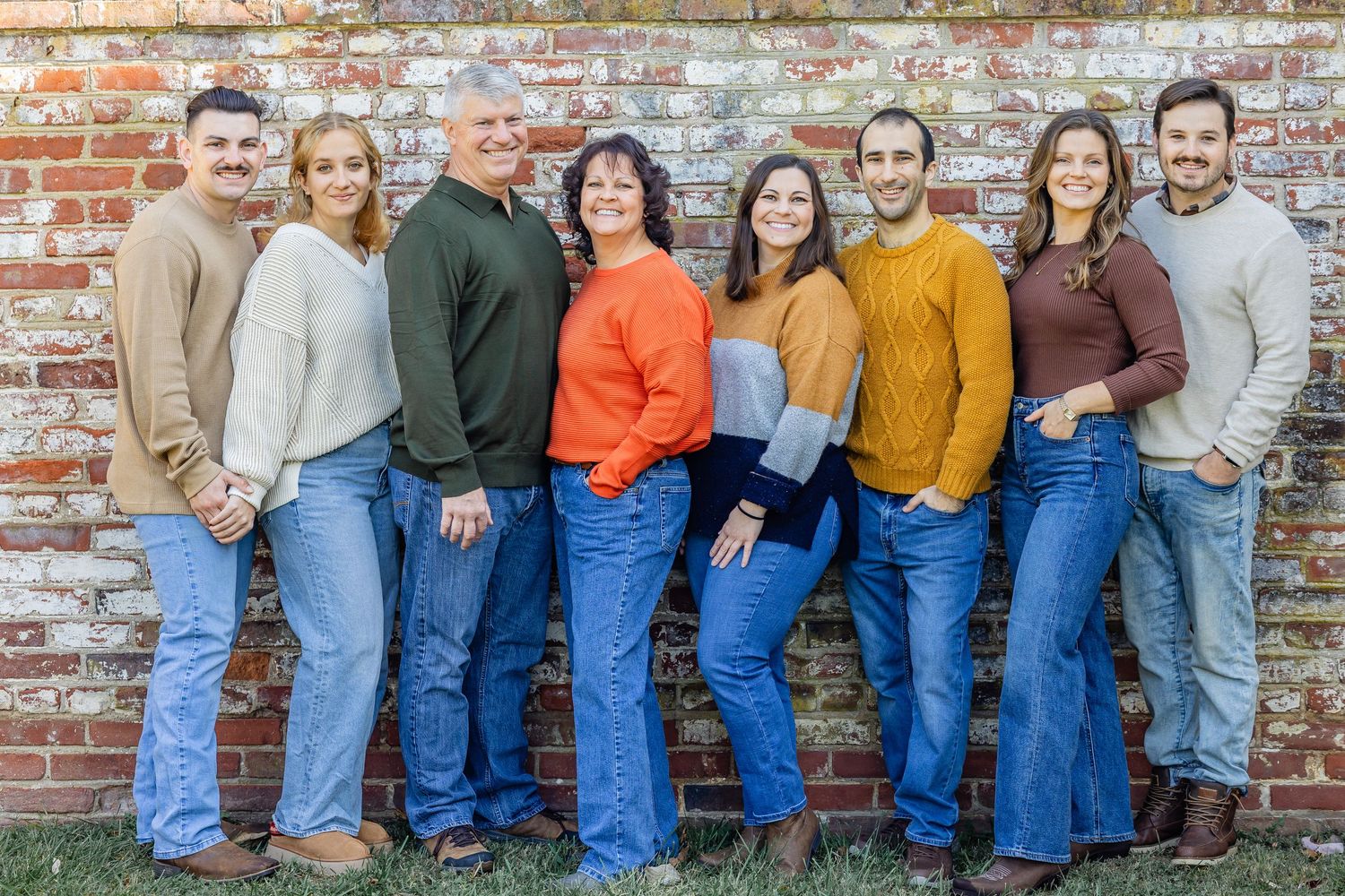 Multi-generational family wearing coordinated denim poses along brick wall.