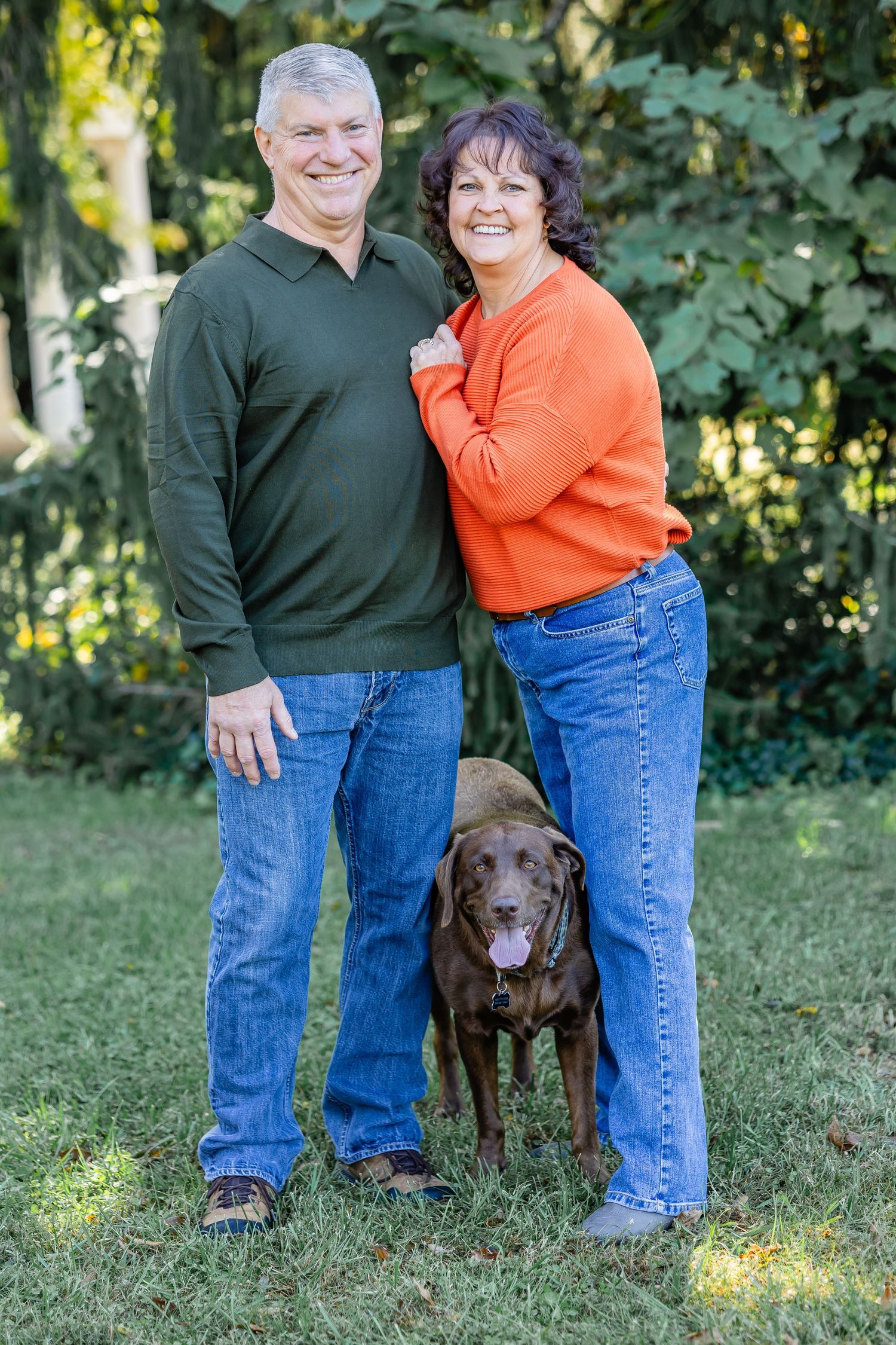Couple with chocolate labrador dog posing together in backyard garden.