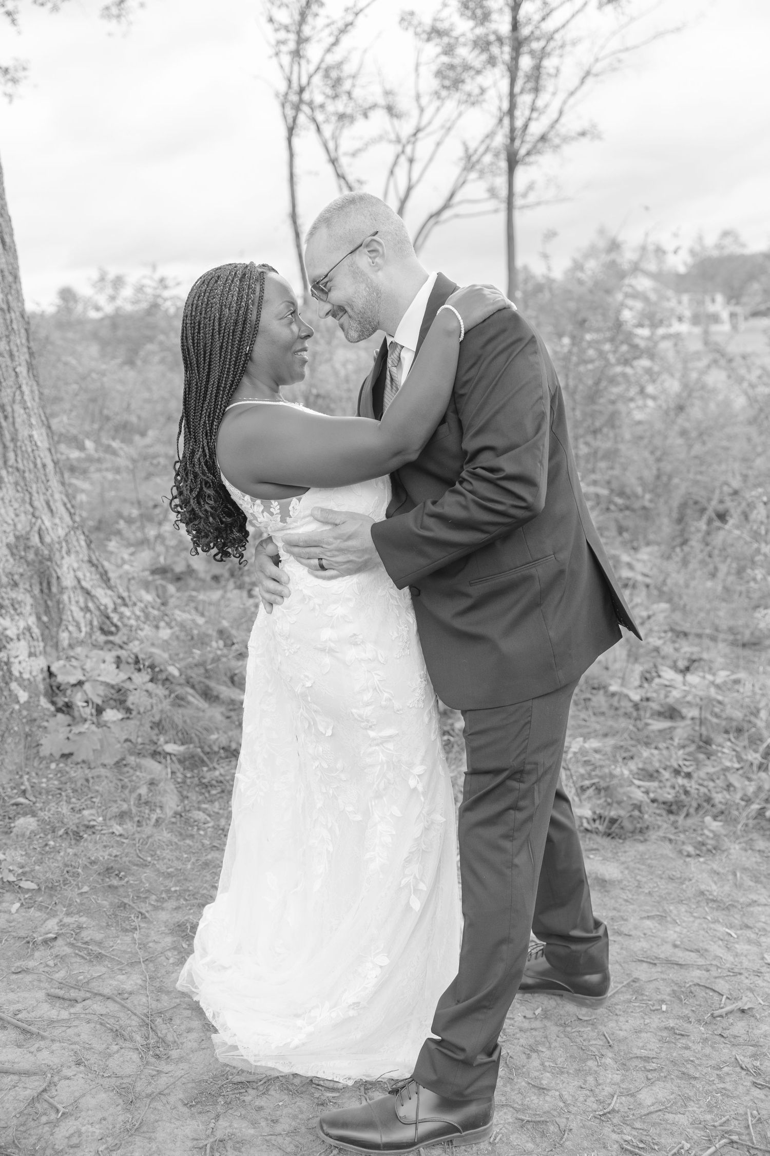 Romantic wedding couple embraces outdoors in black and white photography.