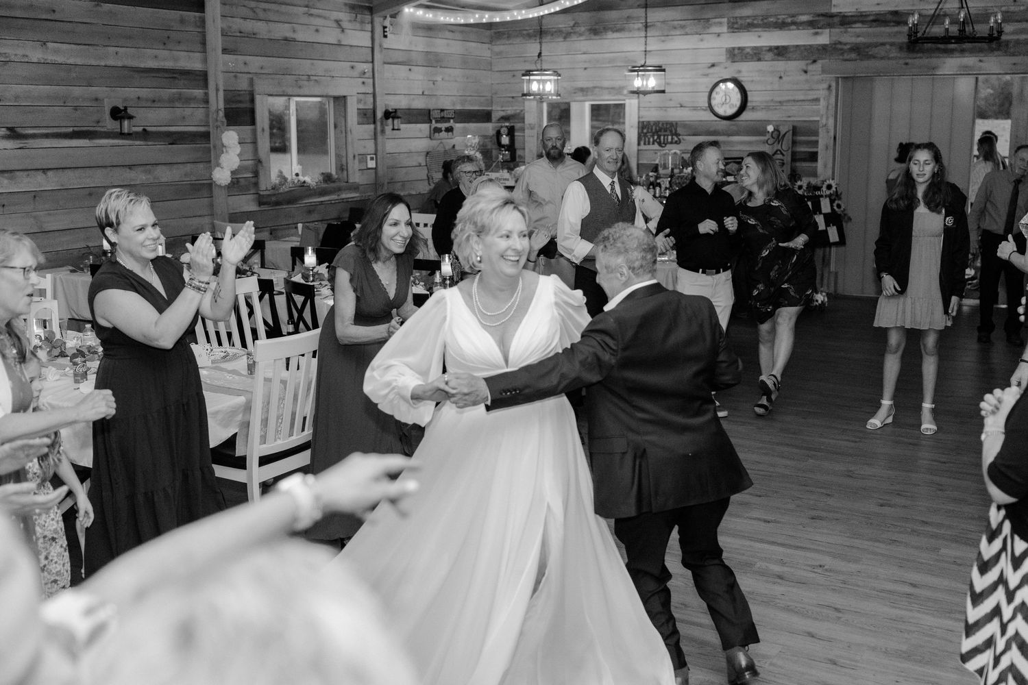 Black and white photo of wedding guests dancing in a rustic barn reception venue.