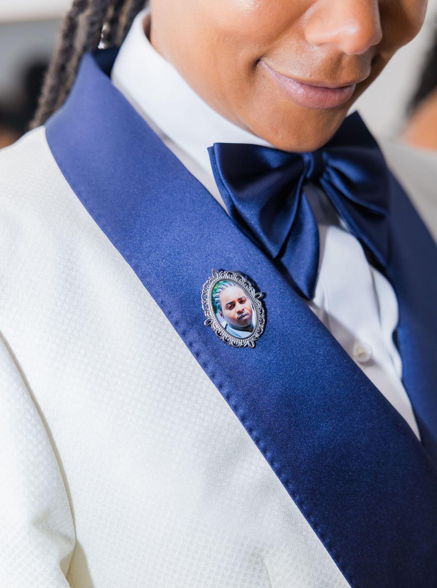 Detail of a navy blue vest with decorative pin against white formal wear.