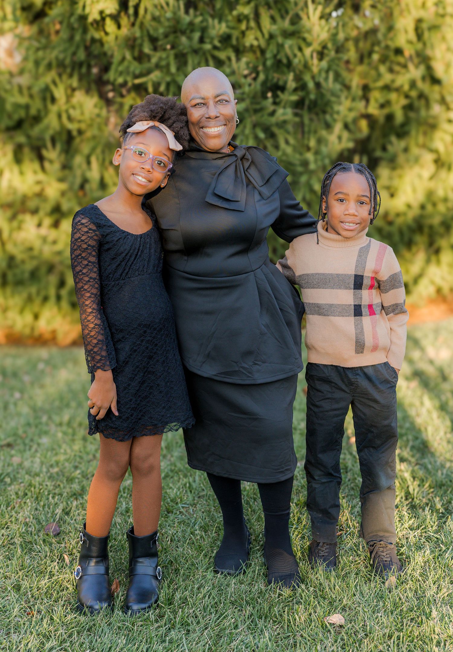 Family portrait of three in coordinated outfits against natural backdrop.