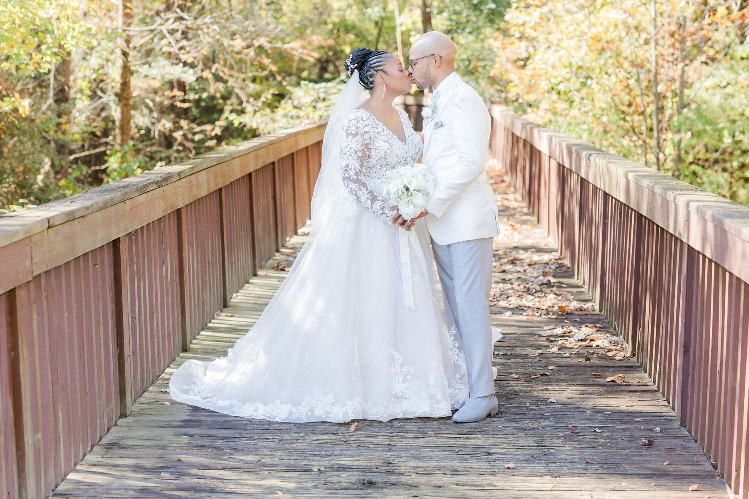 Couple in wedding attire sharing romantic moments on a rustic wooden bridge surrounded by autumn foliage.