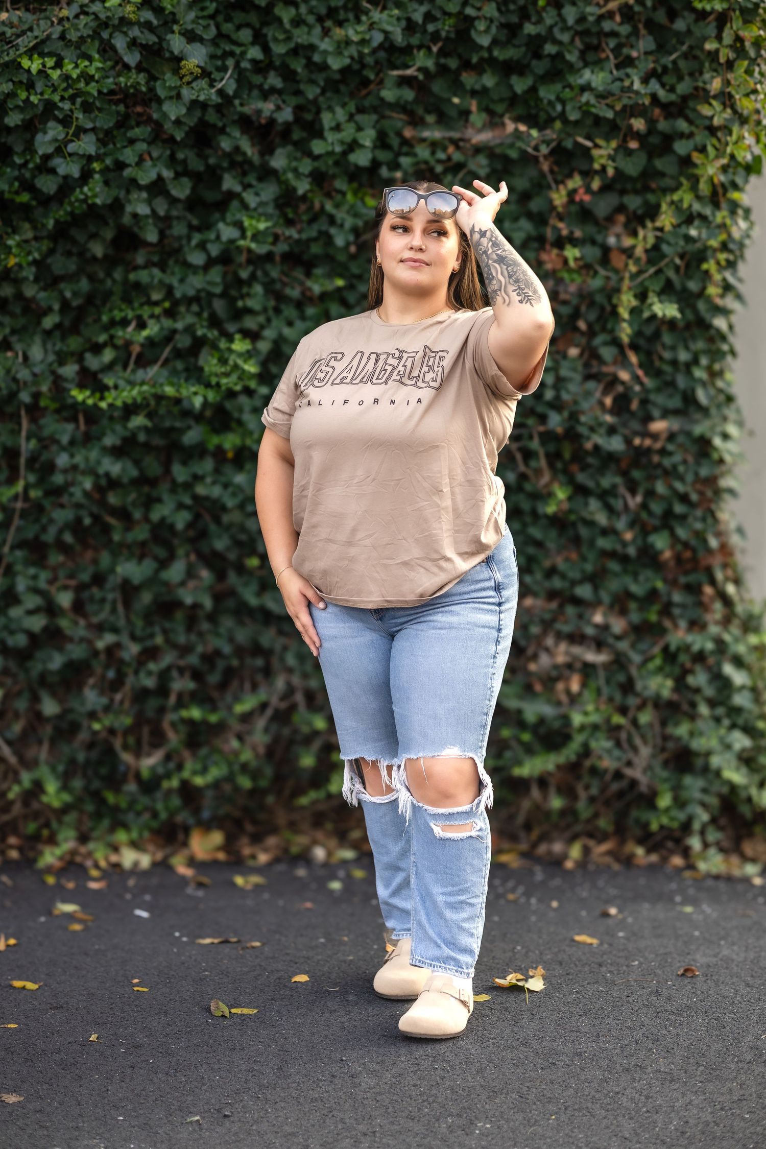 Fashion portrait of woman in casual outfit posing against ivy wall background.