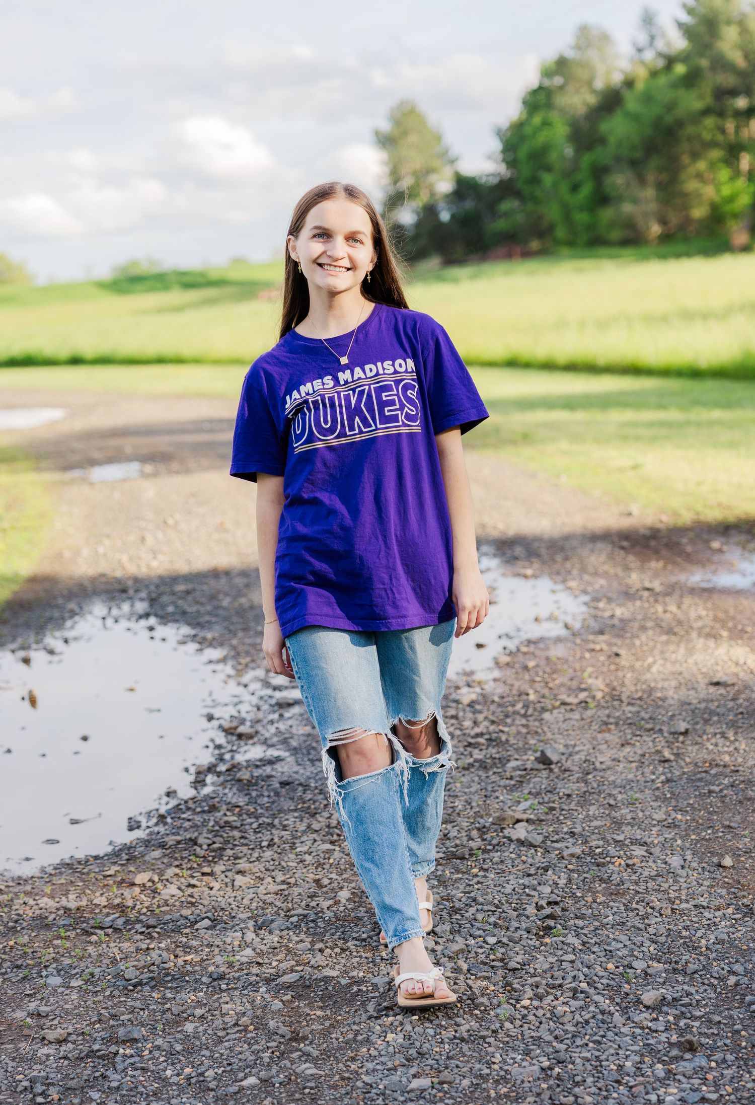 Person wearing purple university t-shirt and distressed jeans walking on gravel path.