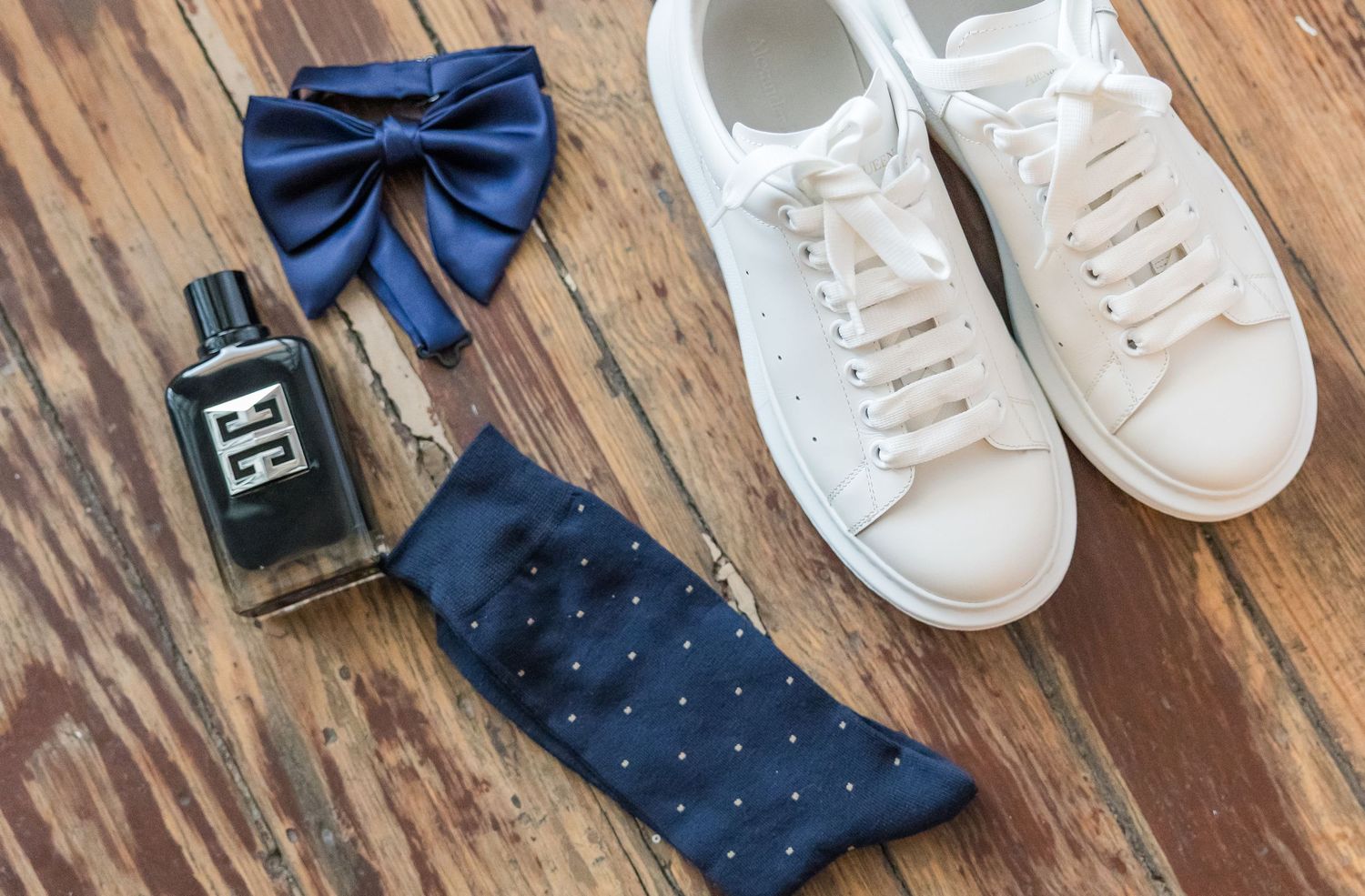 Navy blue bow ties and dress socks arranged with white sneakers on wooden floor.