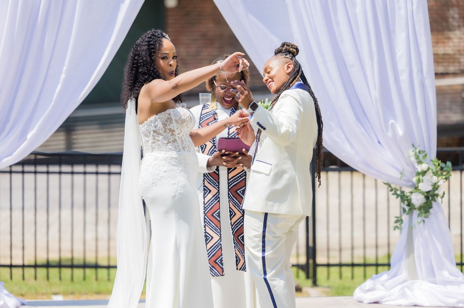 Wedding ceremony with couple and officiant in traditional attire under white draped arch.