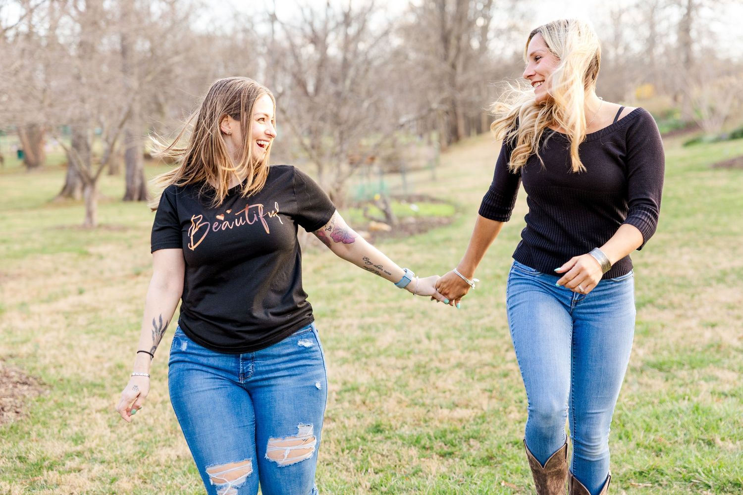 Couple holding hands while walking through scenic field in casual attire.