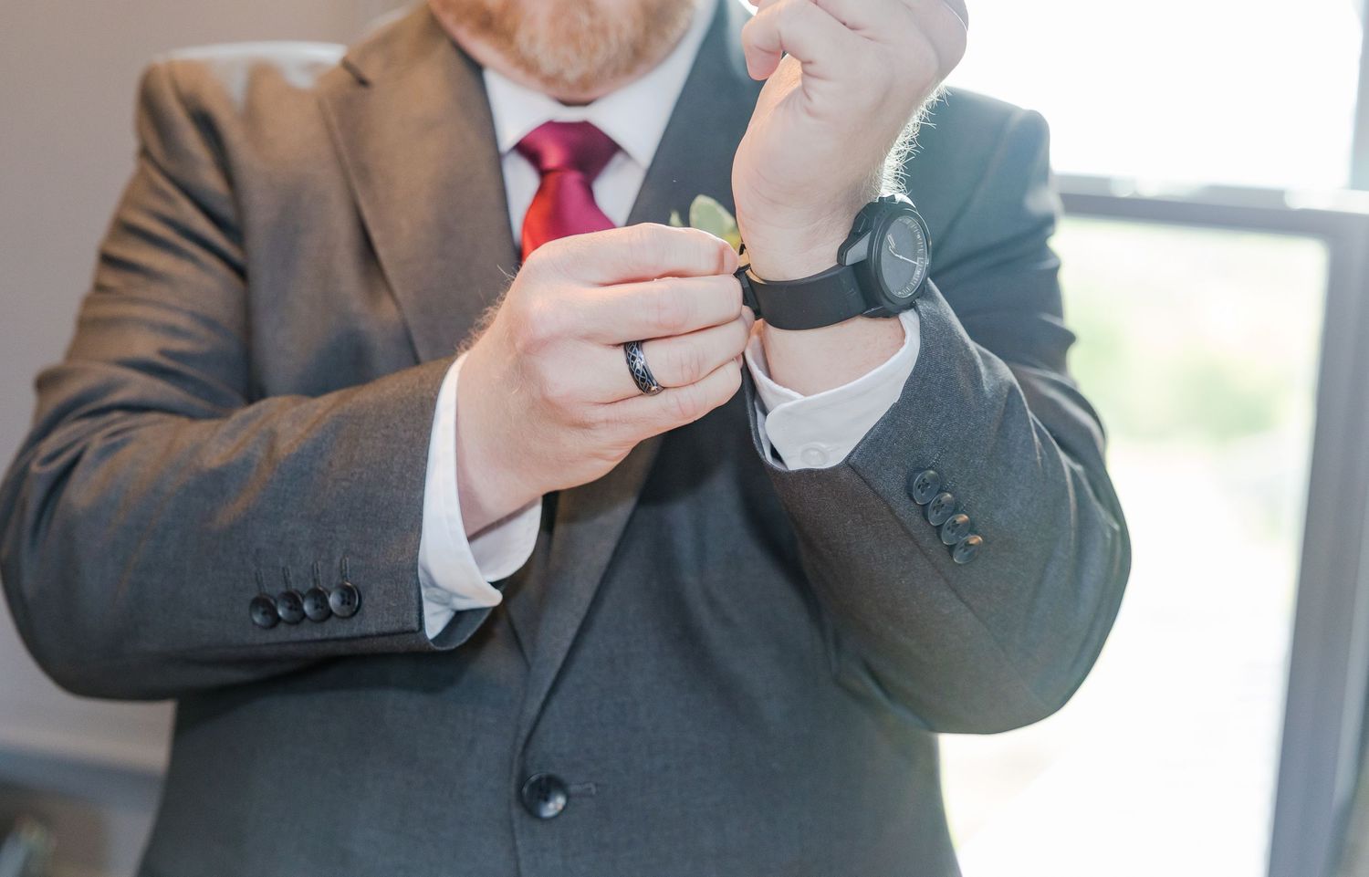 Close-up of hands checking time on a watch while wearing a gray suit and red tie.