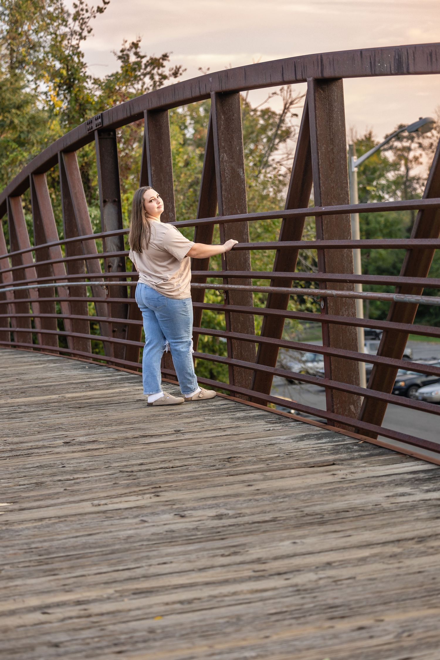 Person walking across wooden bridge during sunset in park setting.